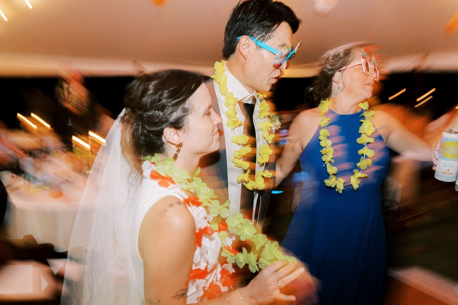 Blurred reception party scene with colorful lei necklaces and dancing.
