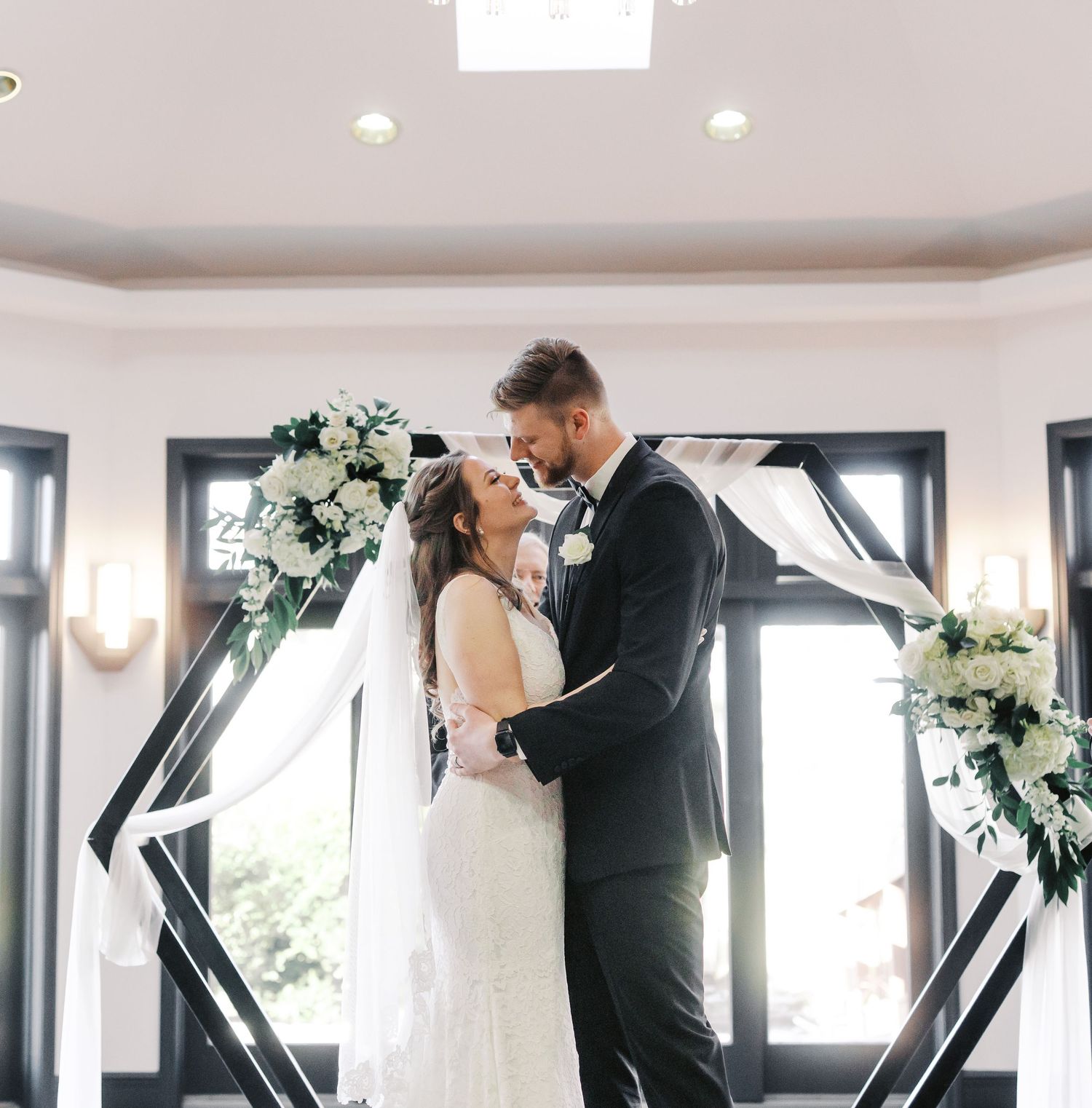 Modern wedding venue space with geometric windows and floral arch decorations.