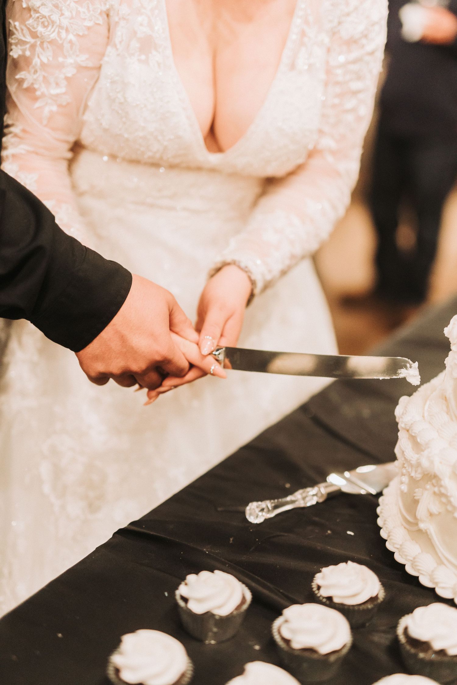 Newlyweds cut their white wedding cake together at reception table decorated with elegant white details.