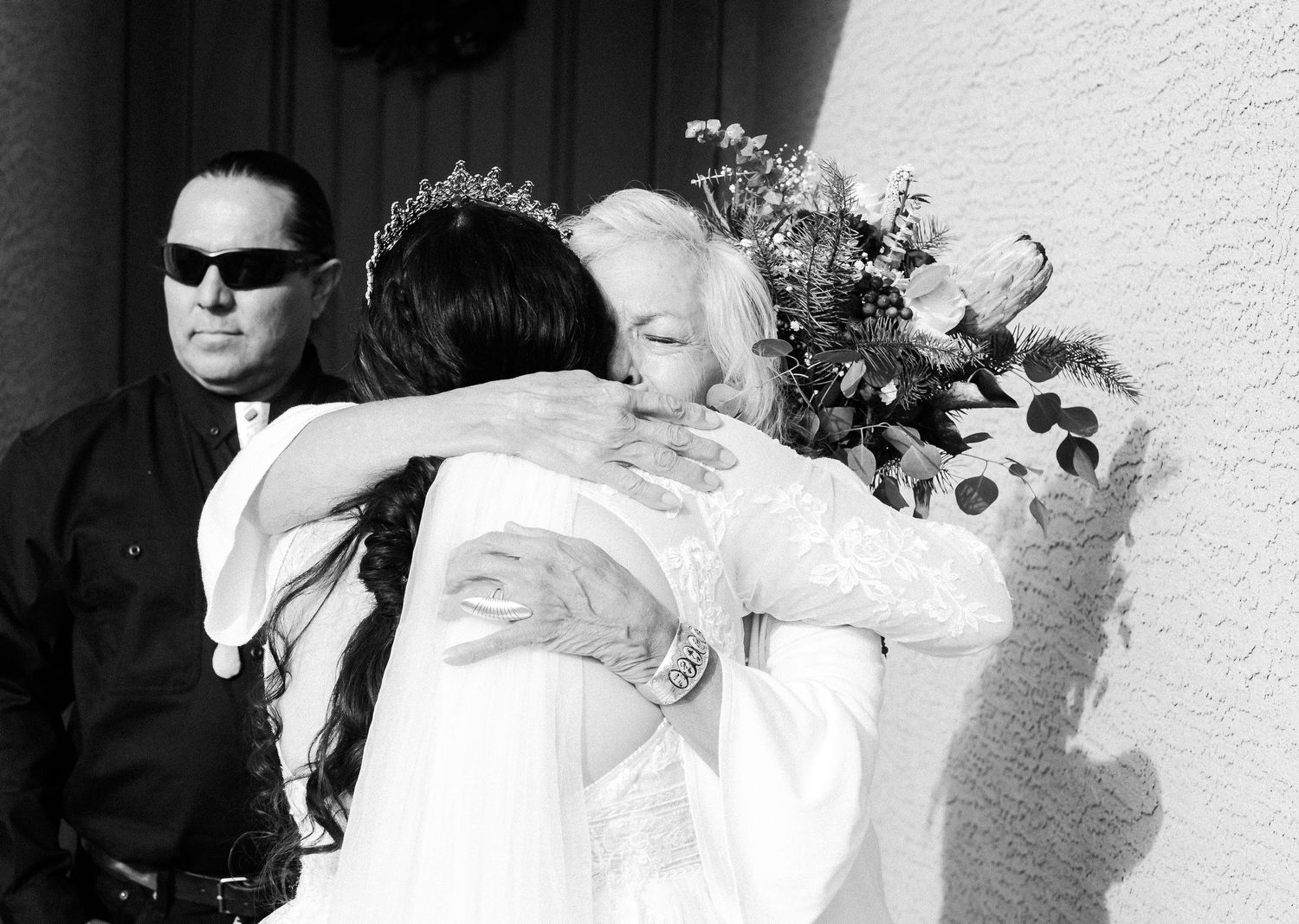 A black and white candid photograph of an embrace at a wedding with sunflowers in the bouquet.