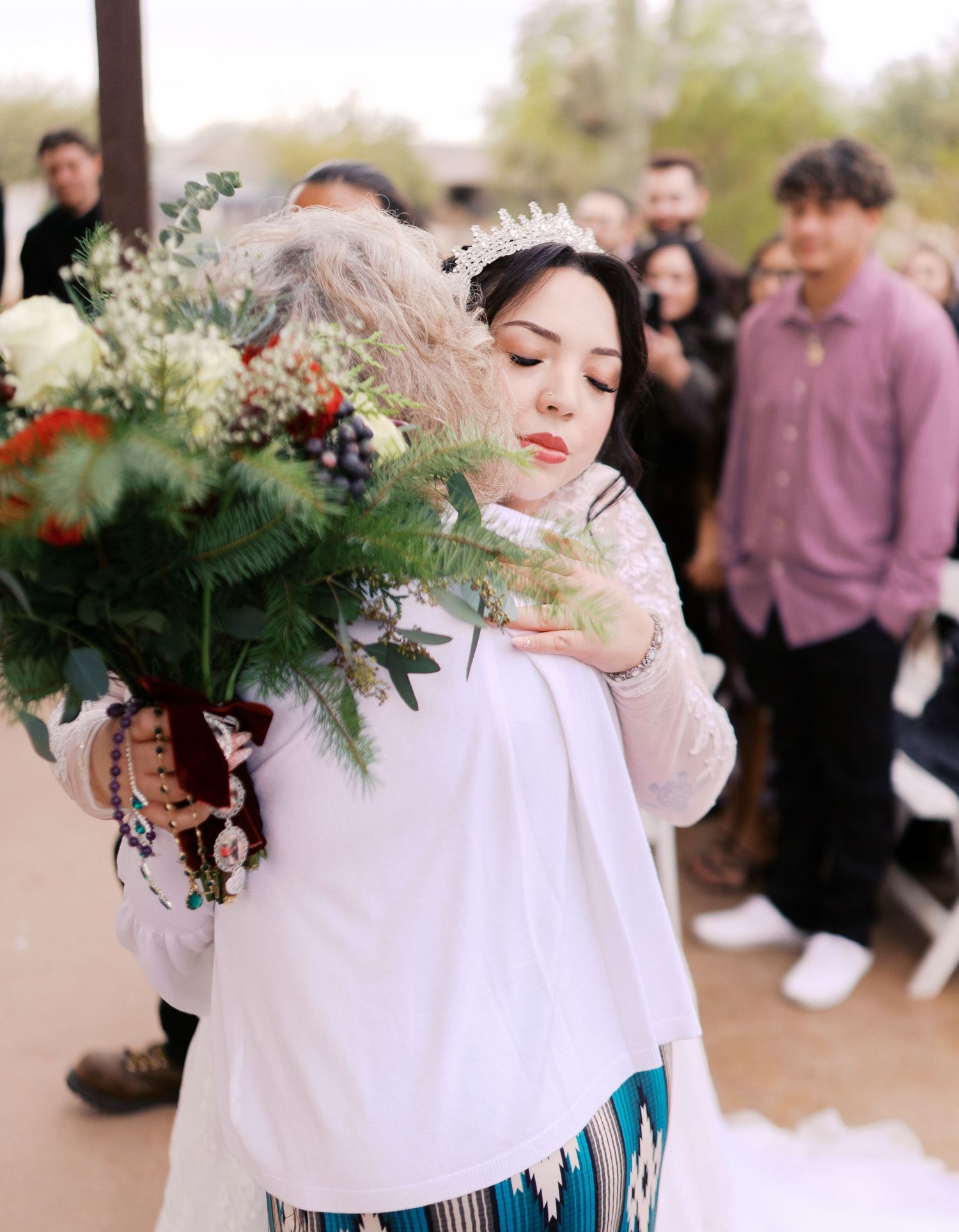A person in a white sweater tenderly examines a beautiful floral bouquet with greenery and blooms against a blurred outdoor background.