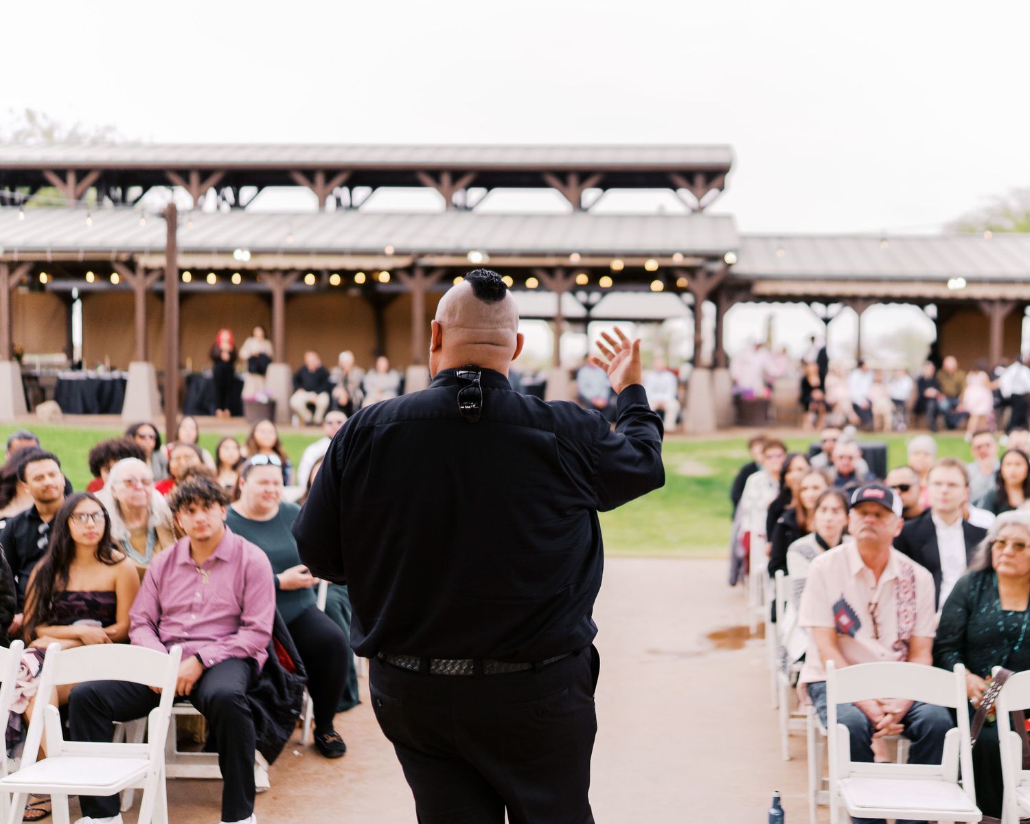 An officiant leads a ceremony in front of seated guests at an outdoor rustic wedding venue.