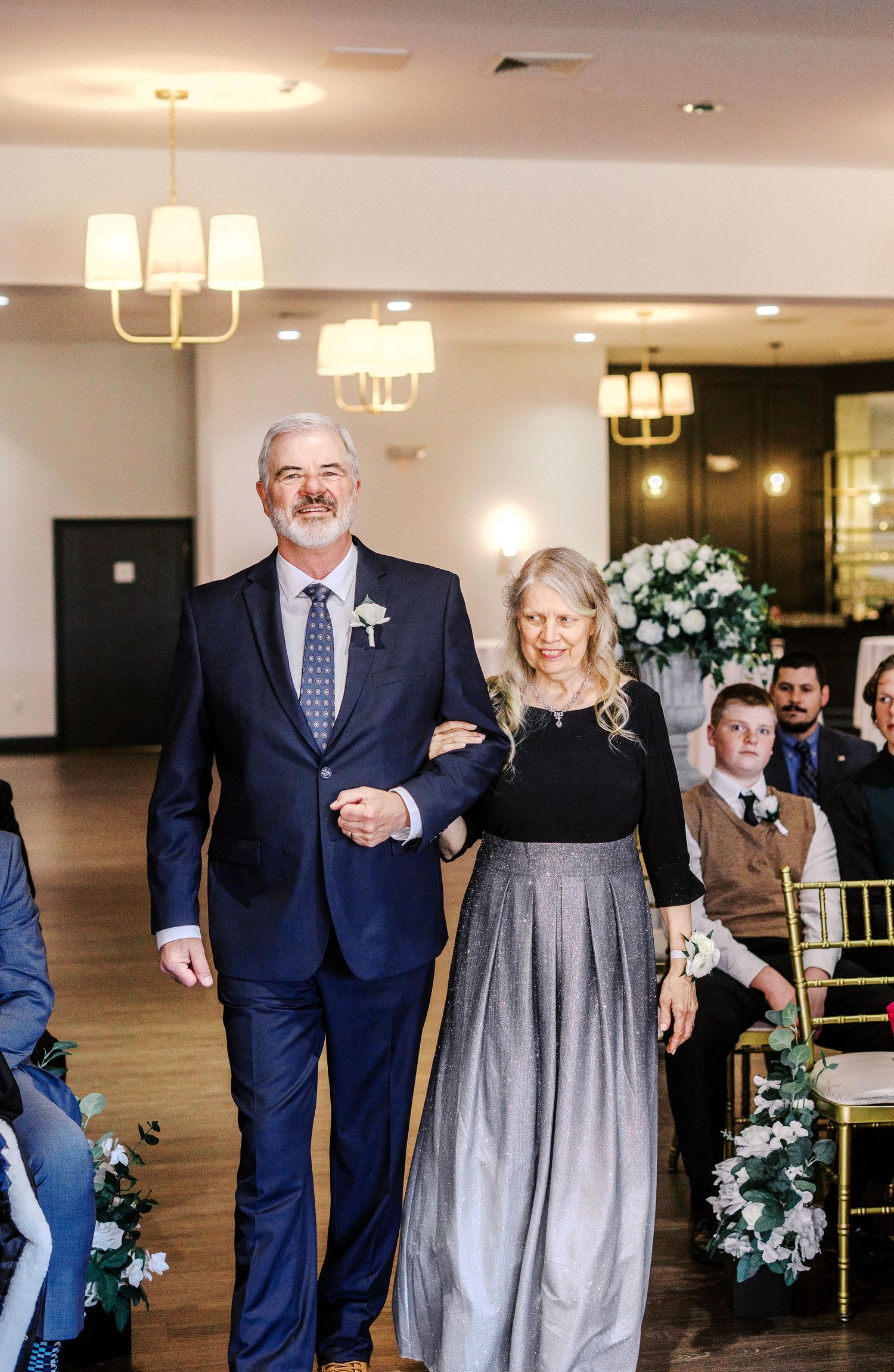 Elegant couple in navy blue and silver attire walk together during a wedding celebration.