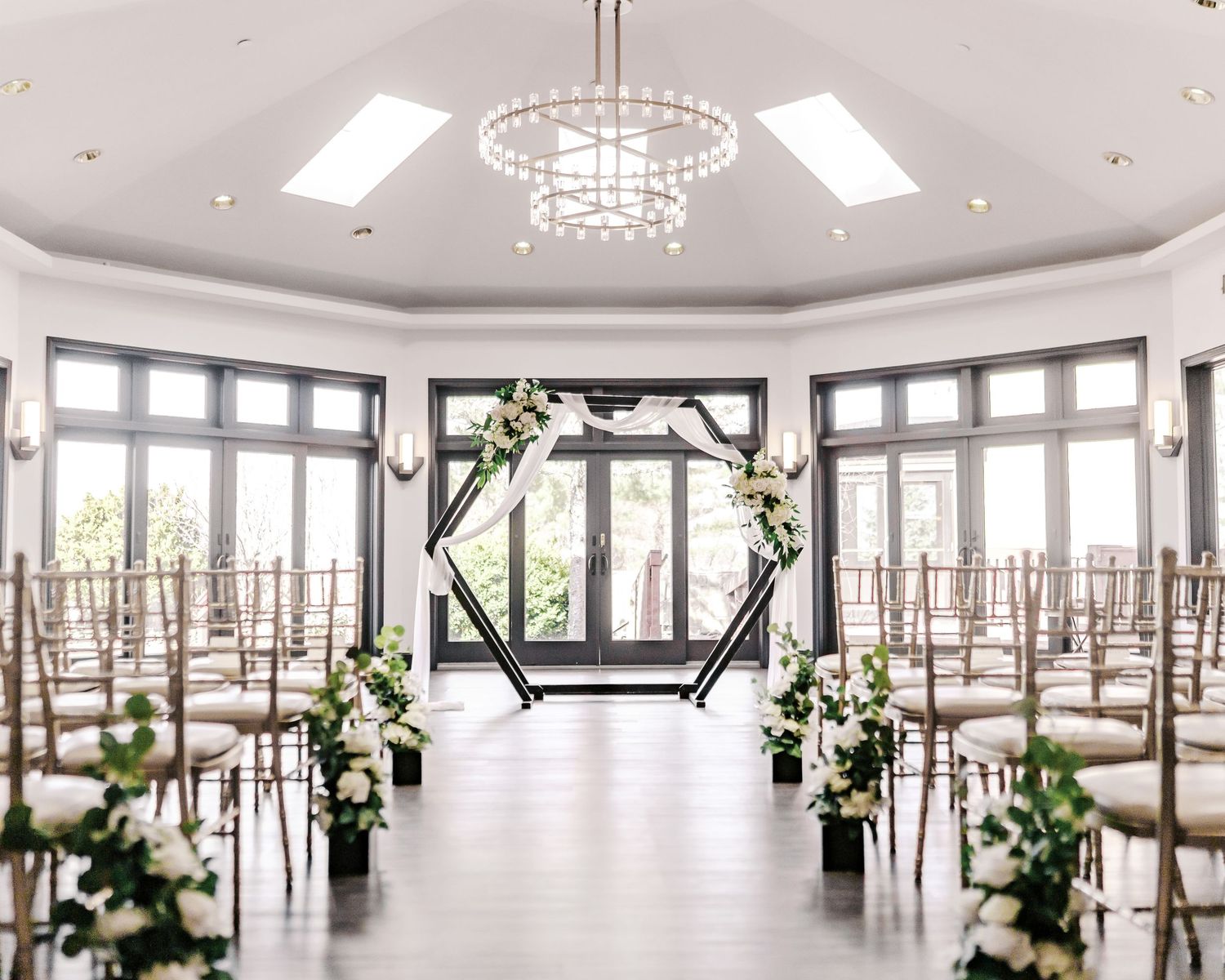 A wide-angle view of an upscale event space featuring crystal chandeliers, tall windows, and decorative white floral displays.