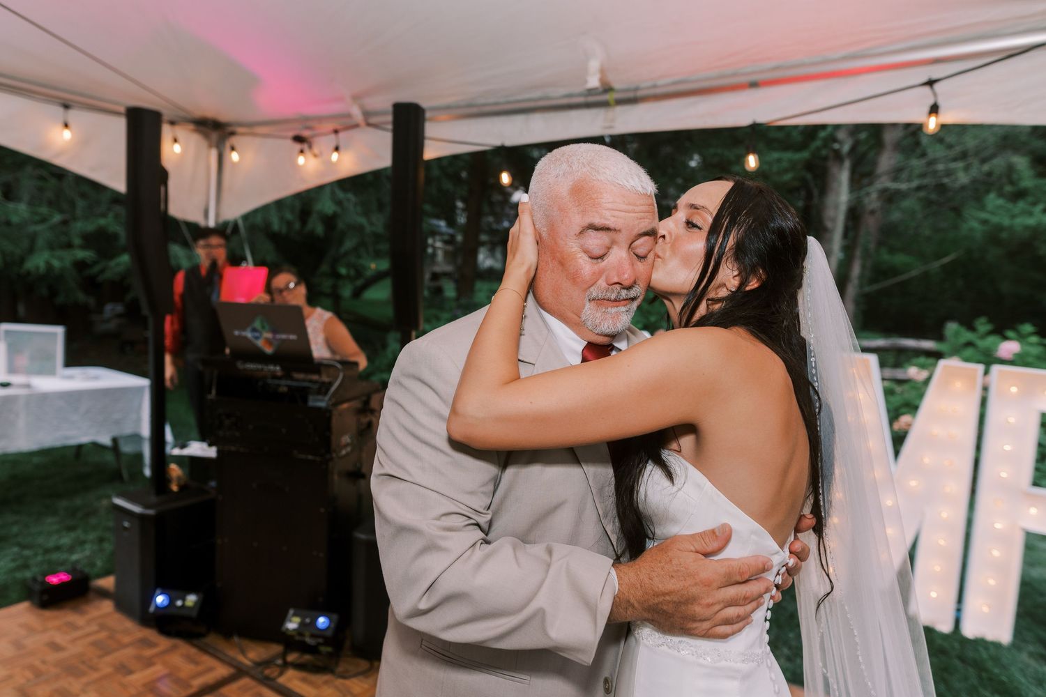 Couples and guests dance and celebrate under a white tent at an outdoor wedding reception.