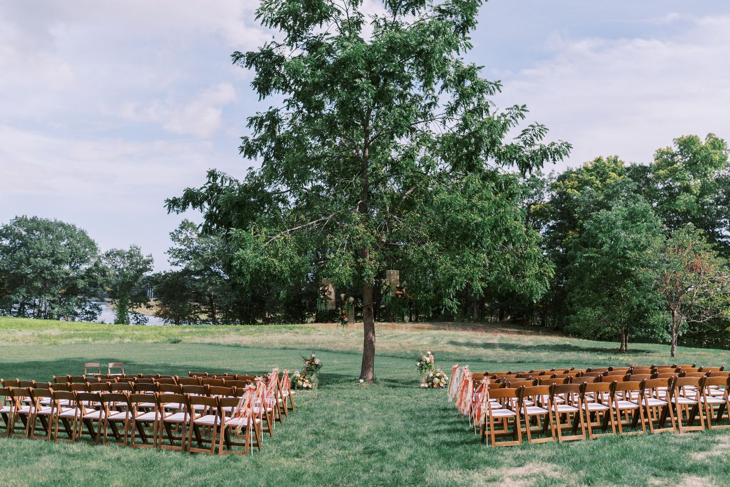 Outdoor wedding ceremony setup with wooden chairs on rolling green hillside.