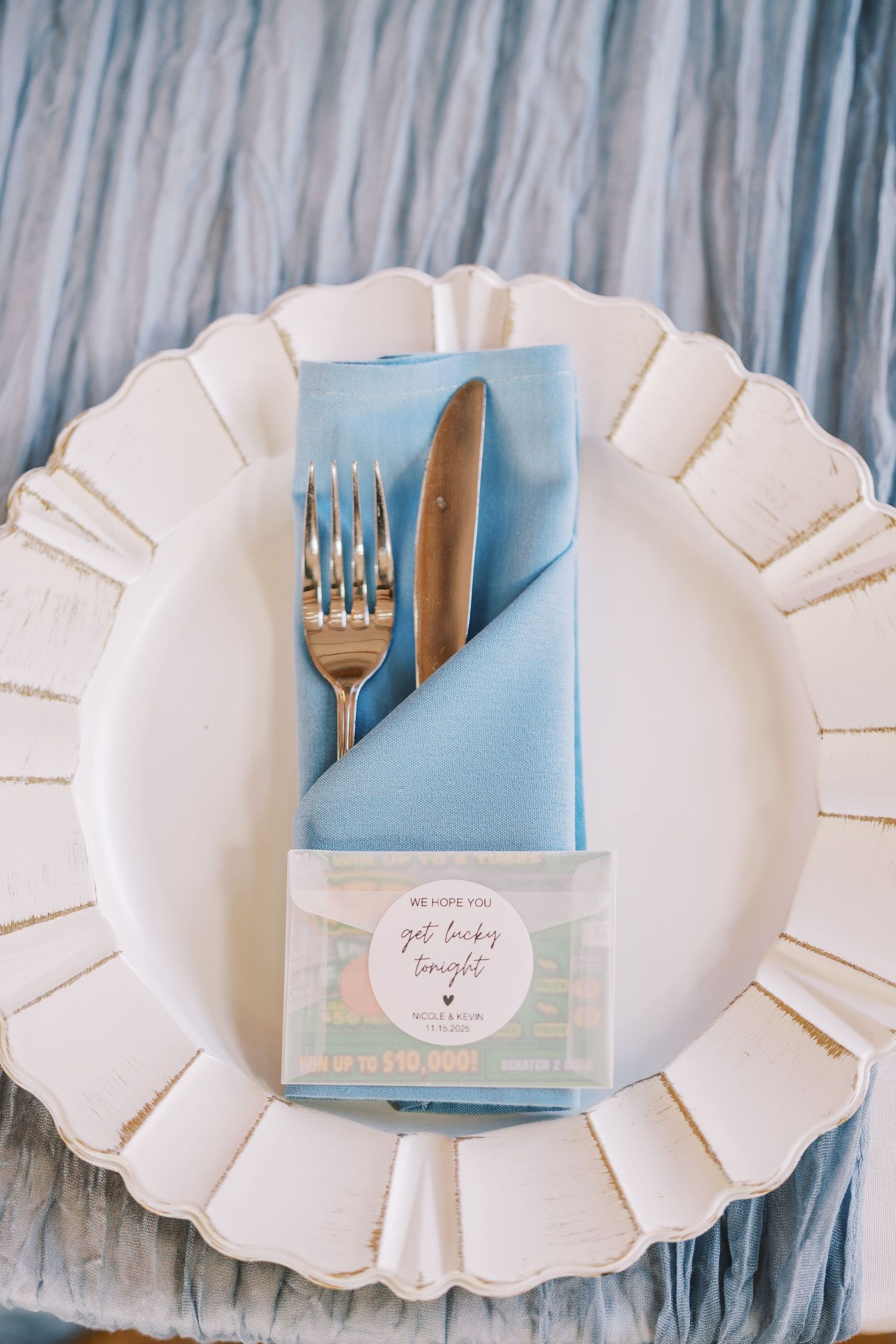 White scalloped paper plates with light blue napkins and silver forks arranged in an elegant table setting display.