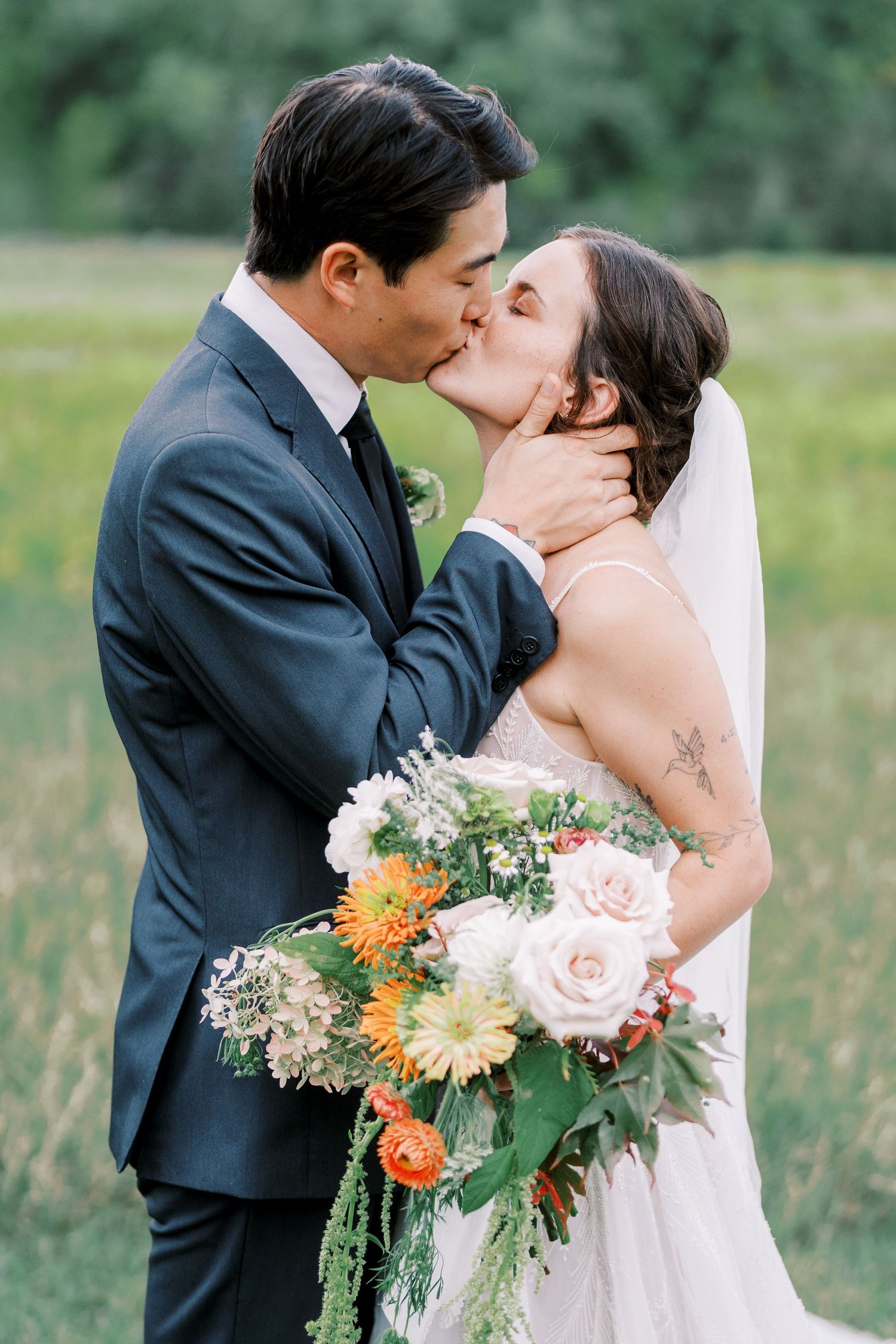 A couple shares romantic wedding photos in a scenic field with lush greenery.