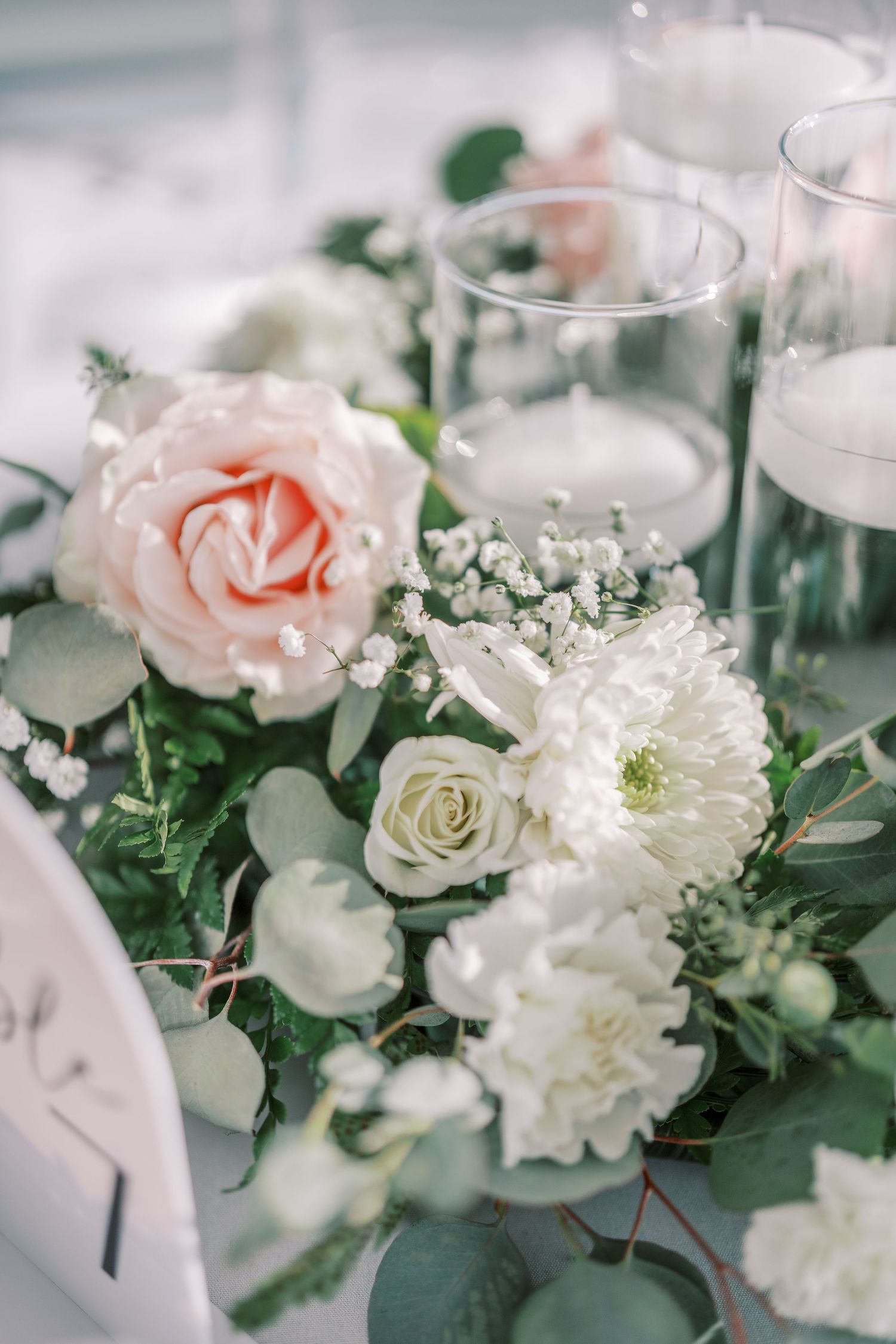 Elegant wedding table centerpiece with soft pink roses, white carnations and baby's breath arranged with greenery.