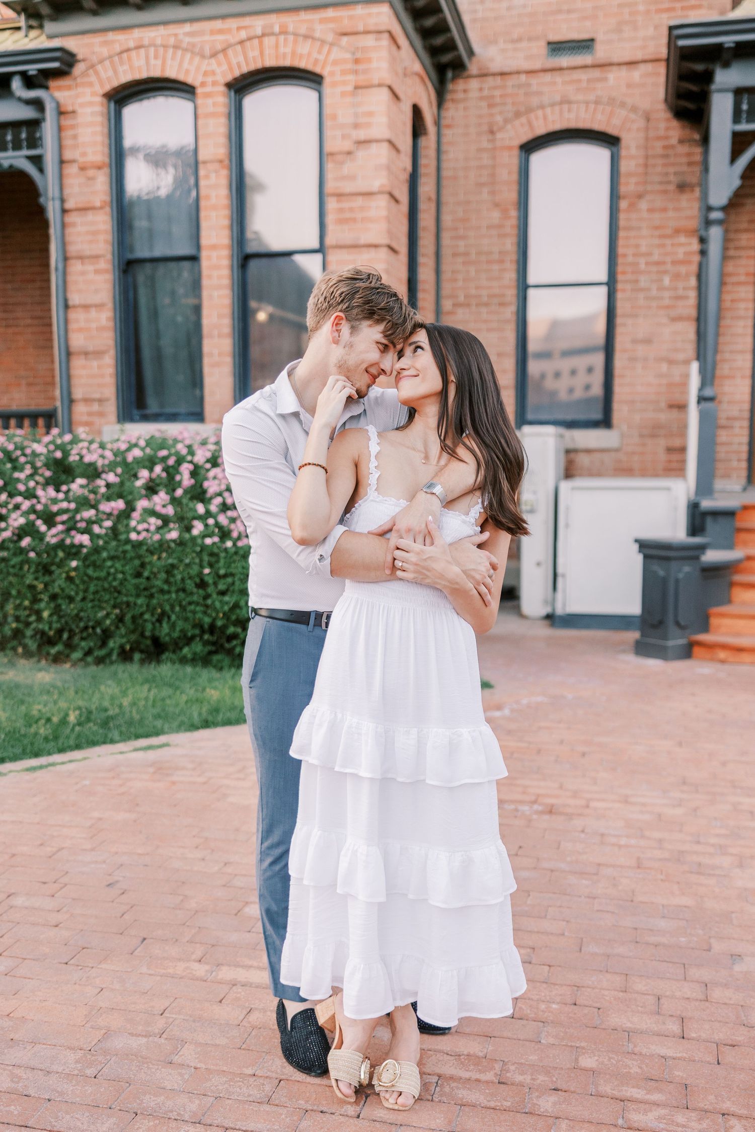 A romantic couple dances together on brick pavement near a historic building with pink roses.