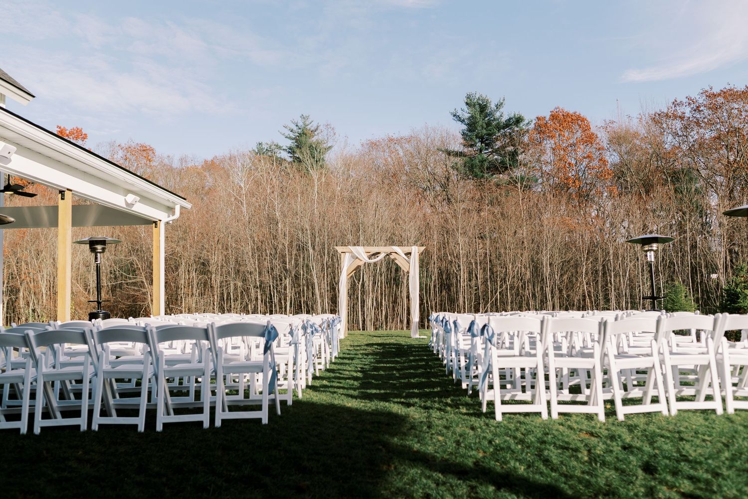 White chairs set up in rows for an outdoor wedding ceremony with evergreen trees and autumn foliage in the background.