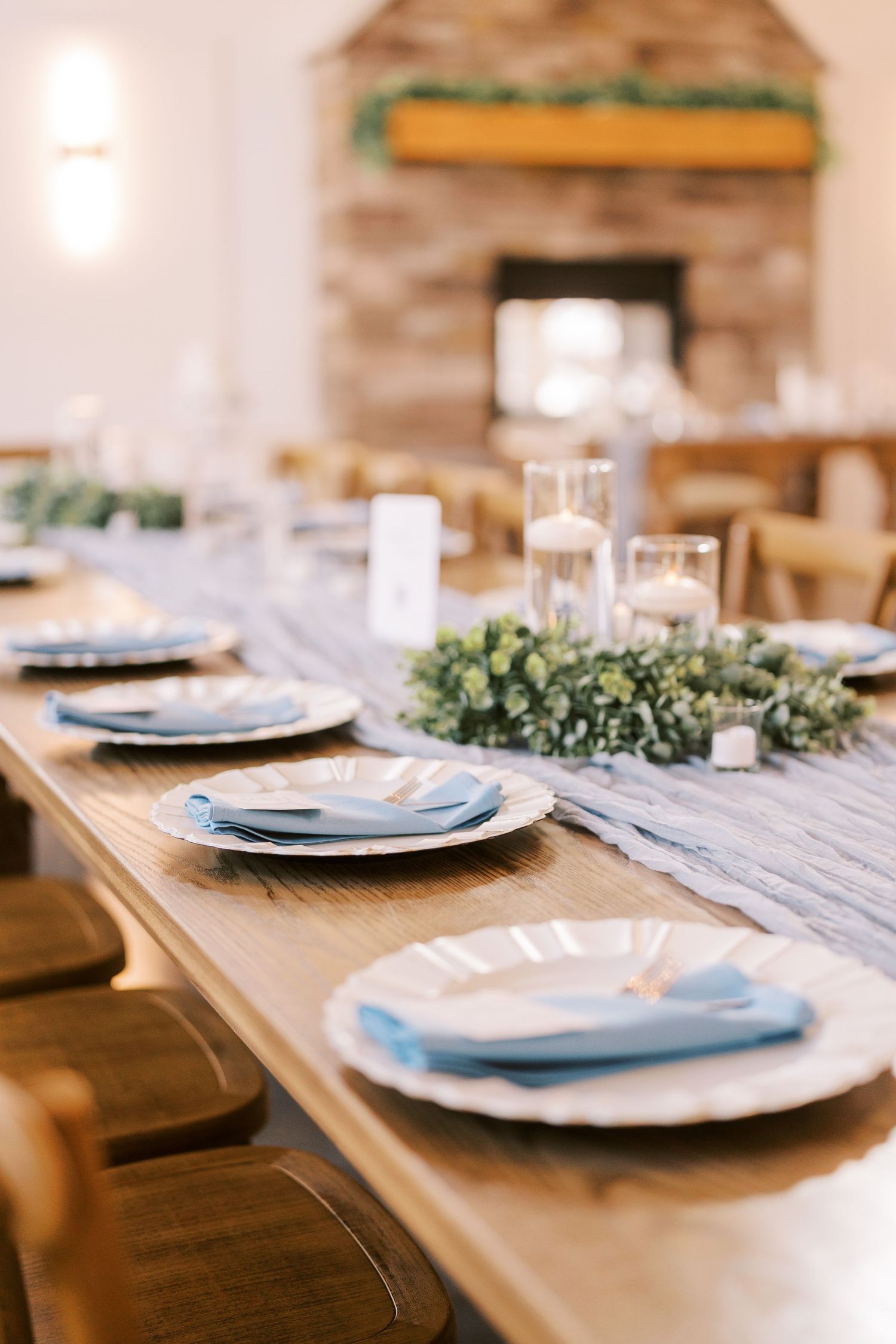 Rustic wooden table set with white plates, blue napkins and greenery garland for elegant wedding reception decor.
