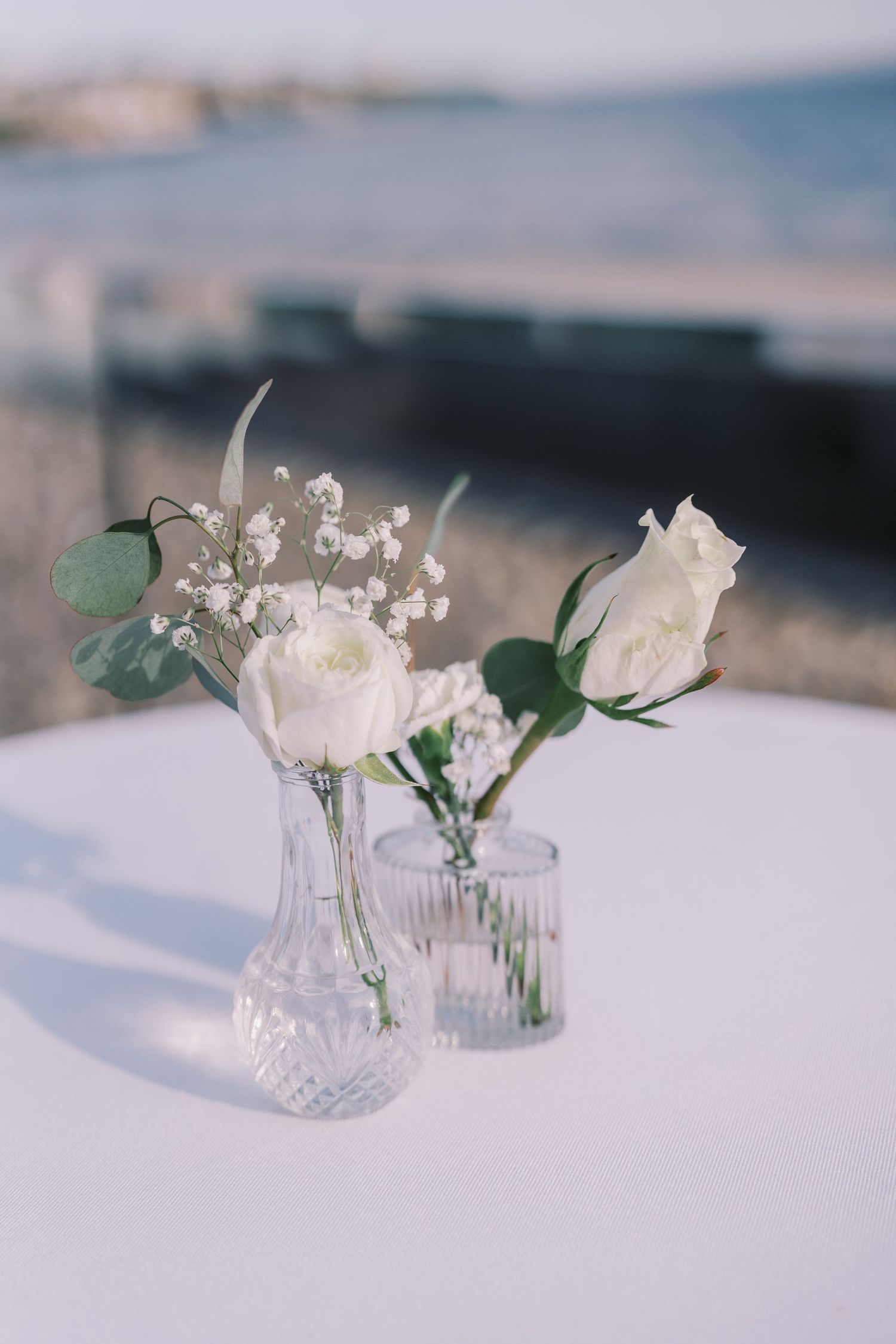 Delicate white flowers arranged in crystal vases on a light blue surface create an elegant table setting.
