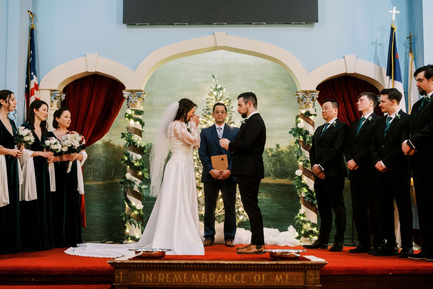 A wedding ceremony takes place in a church with blue walls and decorative floral arches.