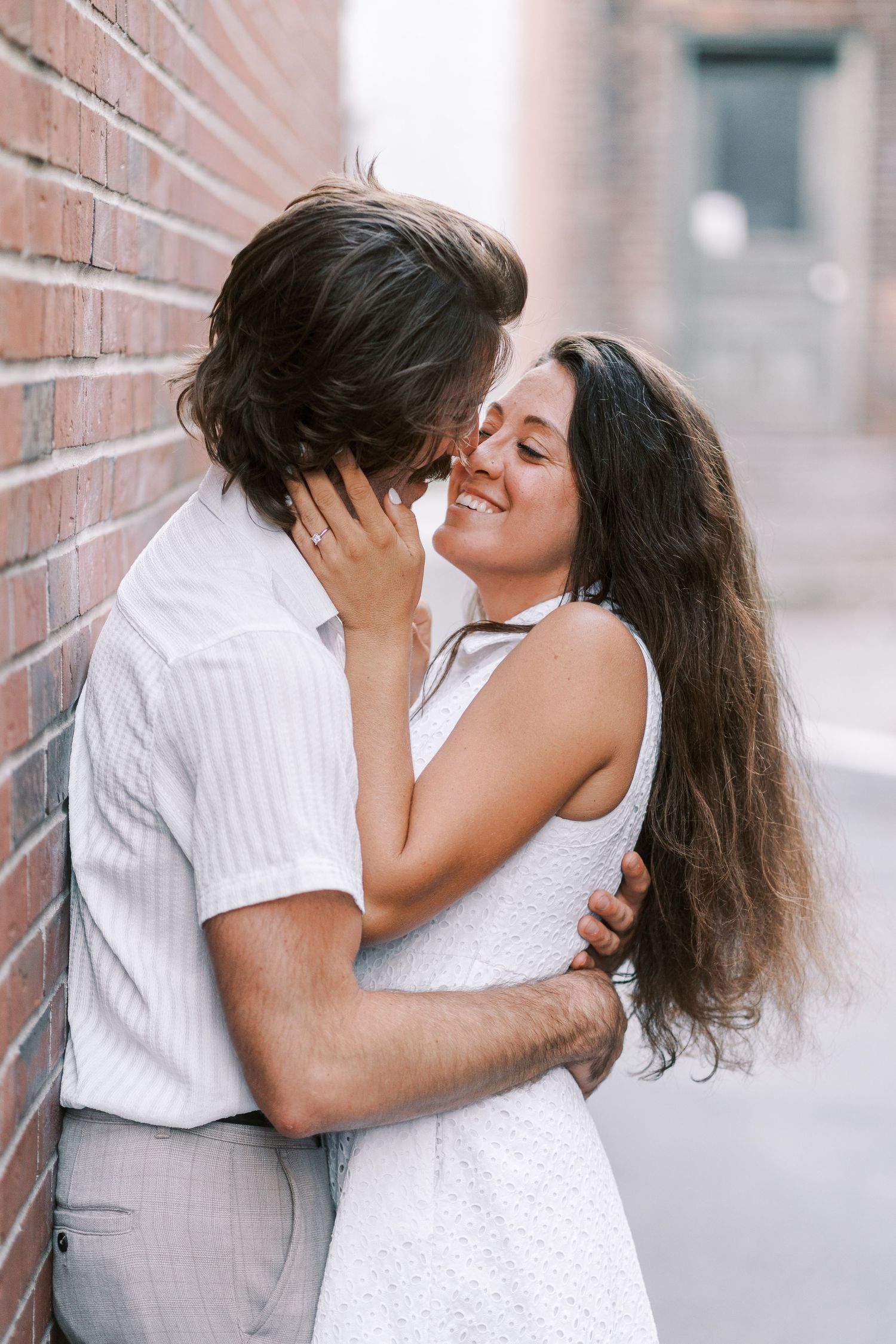 Romantic embrace against brick wall showing joyful expressions.
