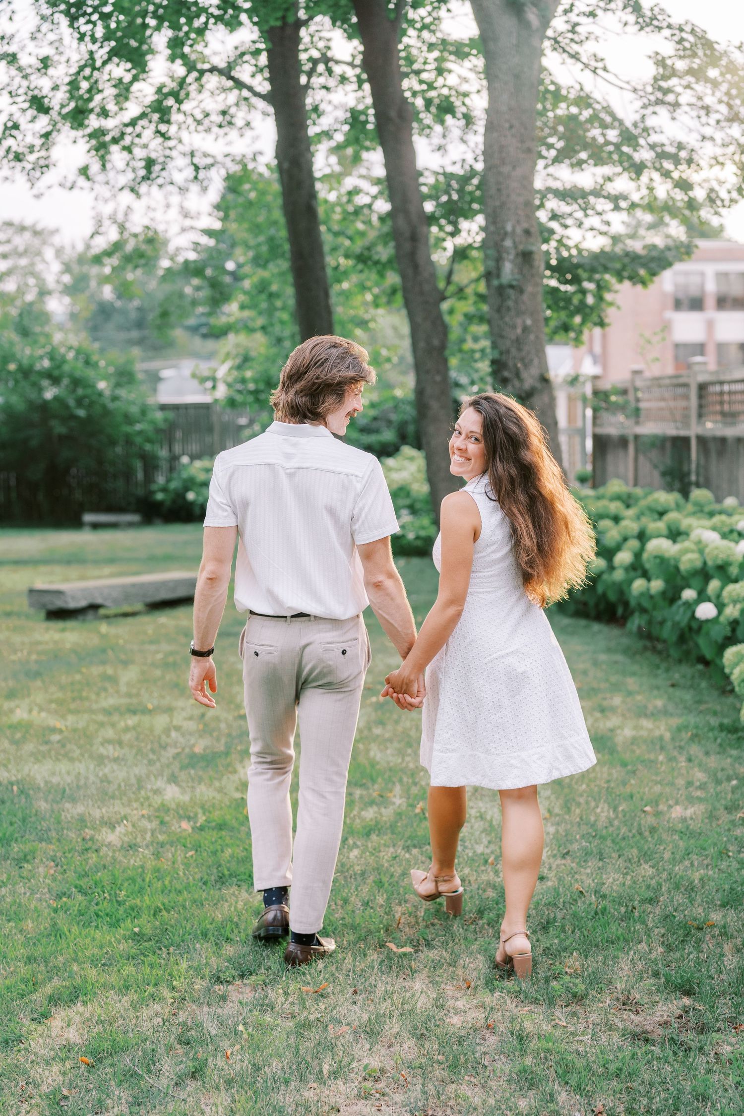 Couple walking hand in hand through a lush garden path on a summer day.