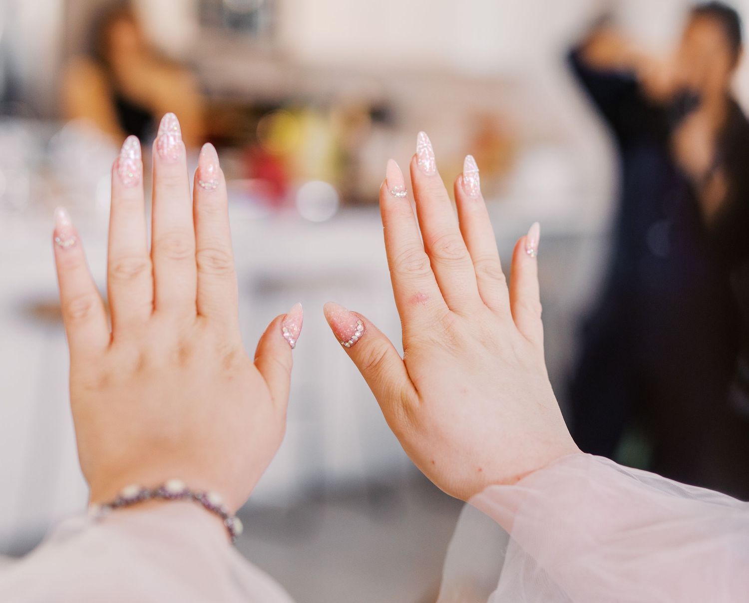 Close-up shot of two hands with long white acrylic nails against a soft blurred background.