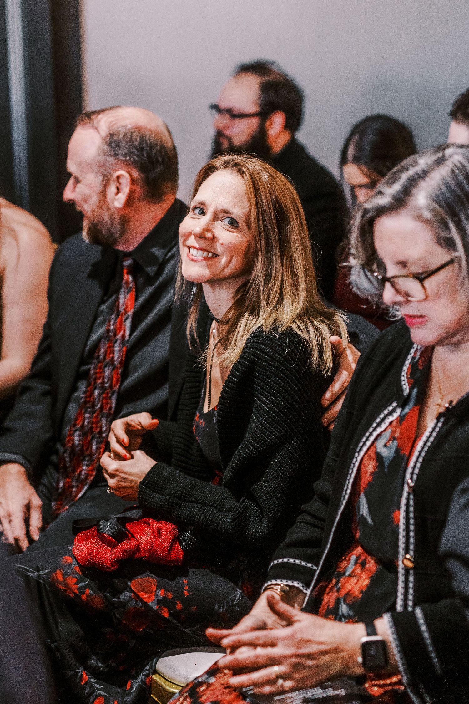 Wedding guests seated in rows wearing black attire with red accents.