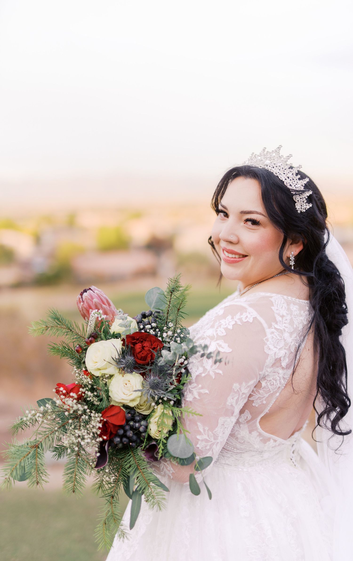 Beautiful wedding bouquet with red and white roses, greenery, and delicate lace details on elegant white bridal gown.