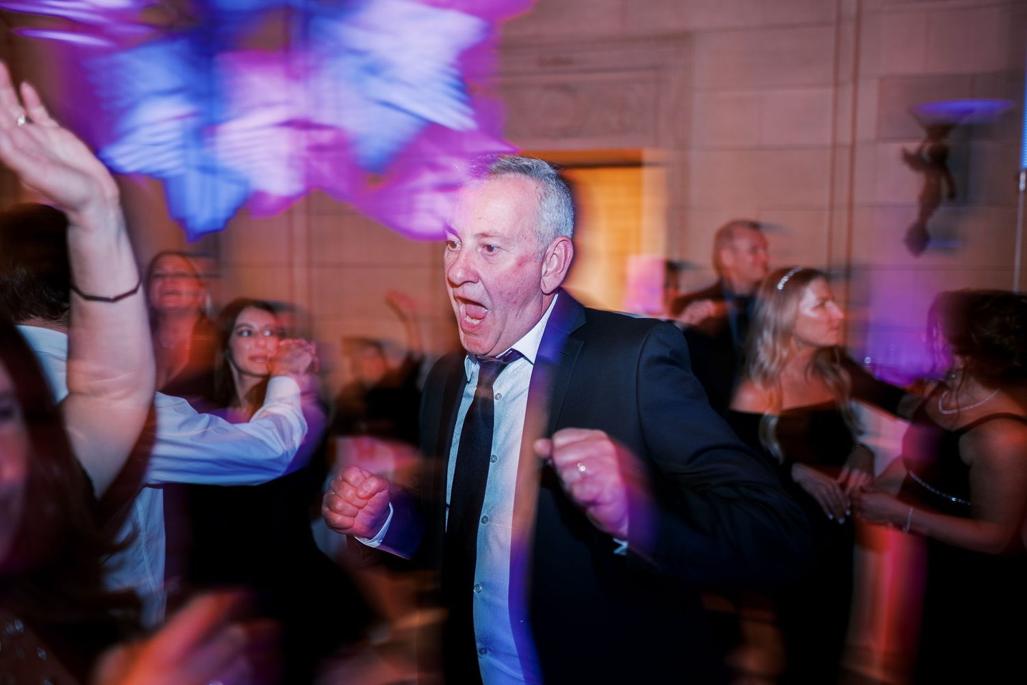 Energetic guest dances enthusiastically on a wedding reception dance floor with colorful purple lighting effects.