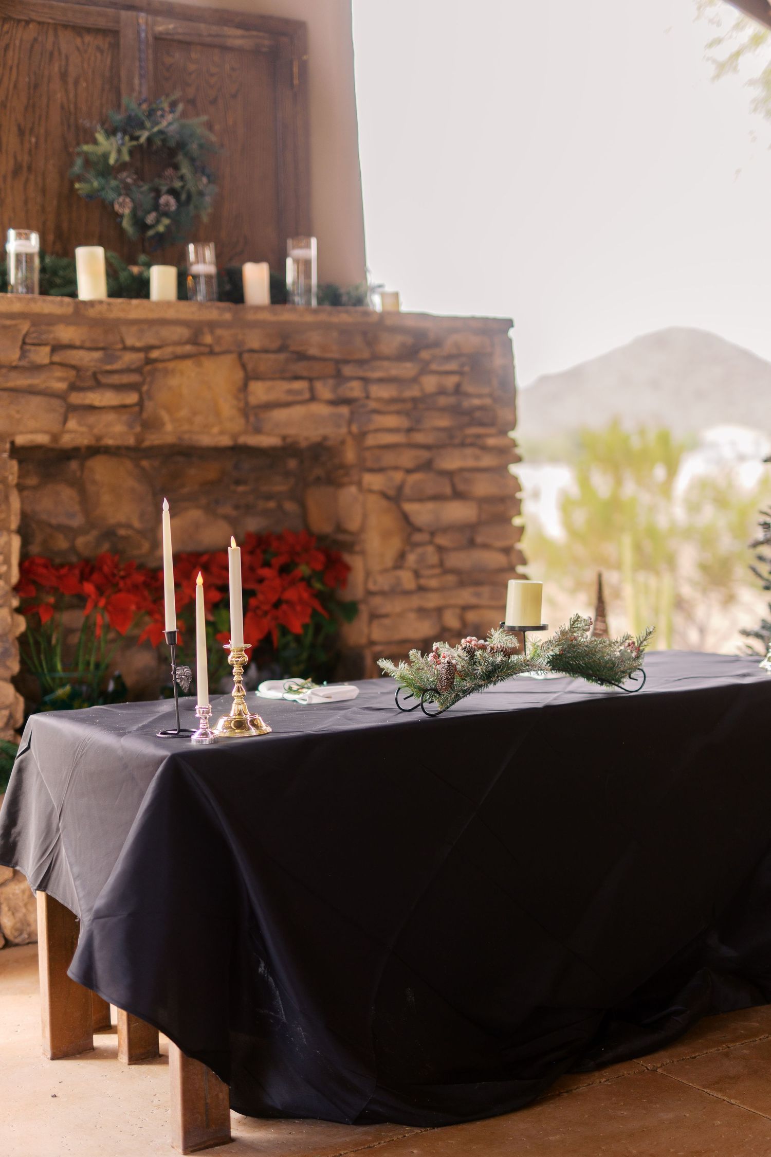 Elegant wedding table with black tablecloth, white candles and red poinsettias against stone fireplace with holiday wreath.