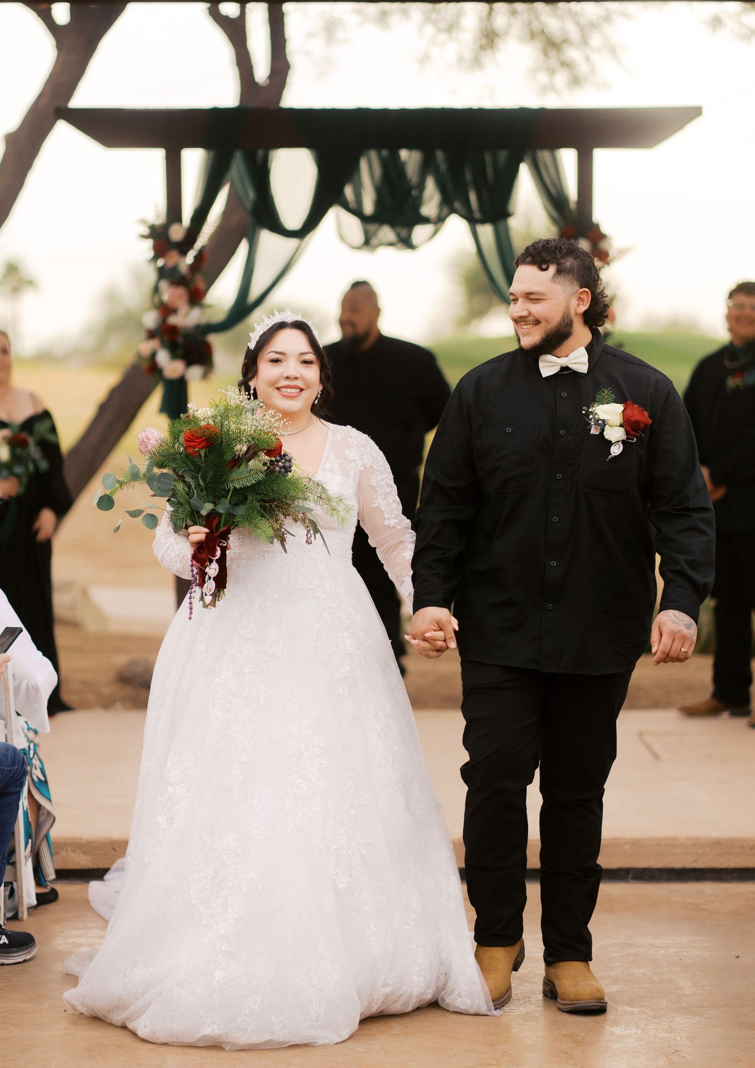 Newlyweds walk hand in hand under decorated outdoor wedding arch.
