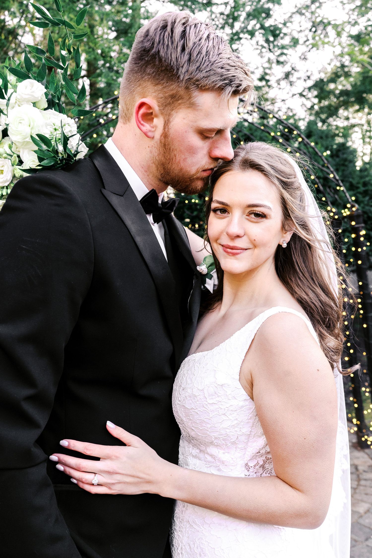 A serene outdoor portrait sequence of a couple in formal wedding attire embracing among trees and string lights.