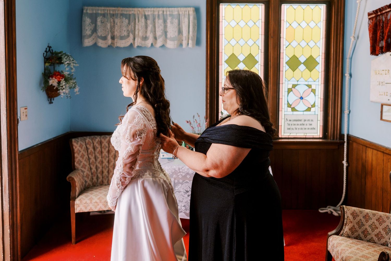 Wedding party helps bride prepare in a room with blue walls and wooden wainscoting.