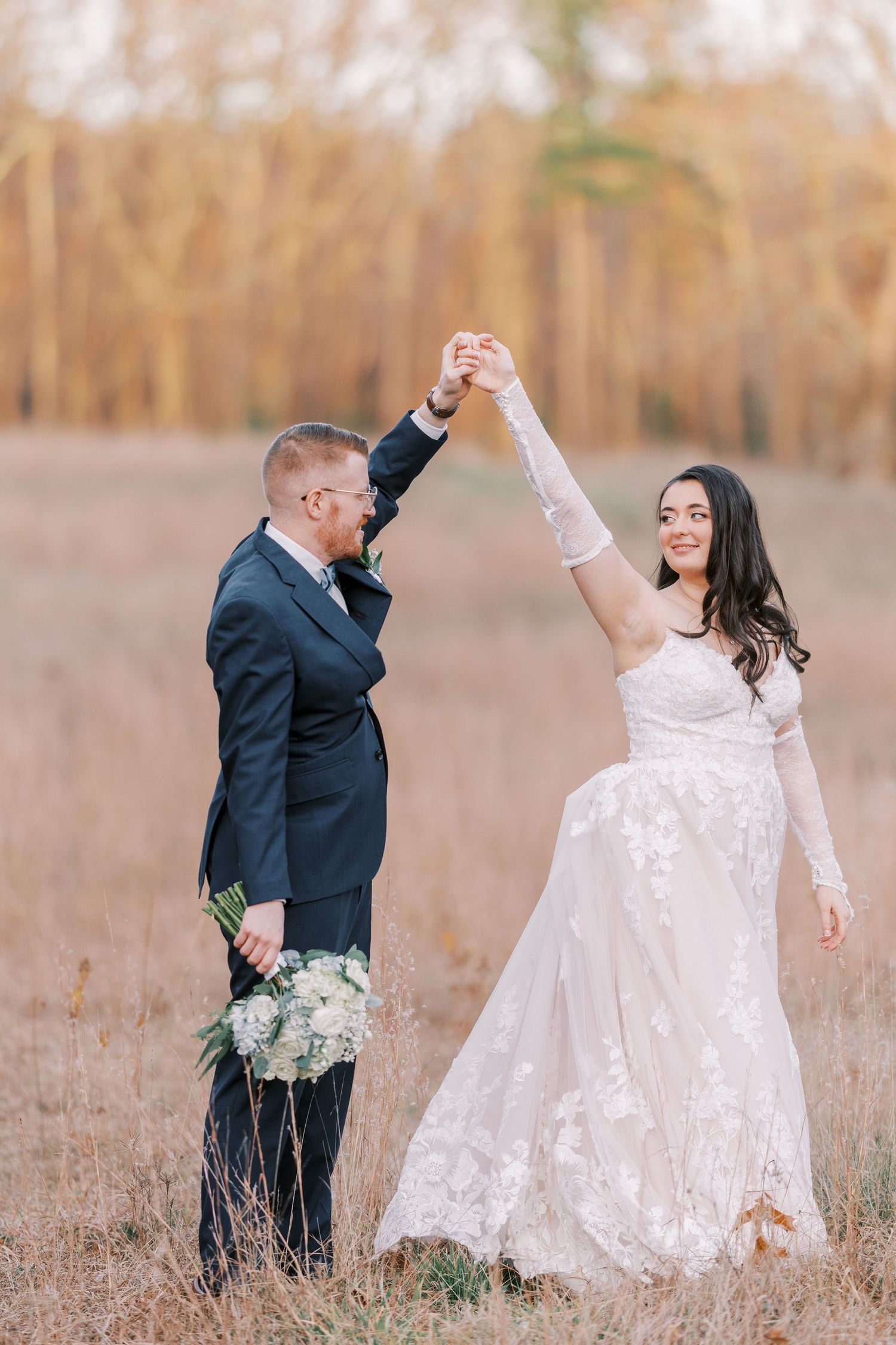 A couple in wedding attire dance together in a golden field during sunset, creating a romantic and joyful scene.