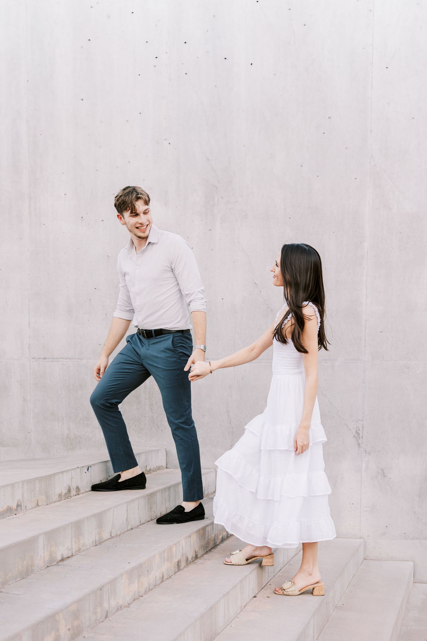 Couple playing and posing on white concrete steps in coordinated white and blue outfits.
