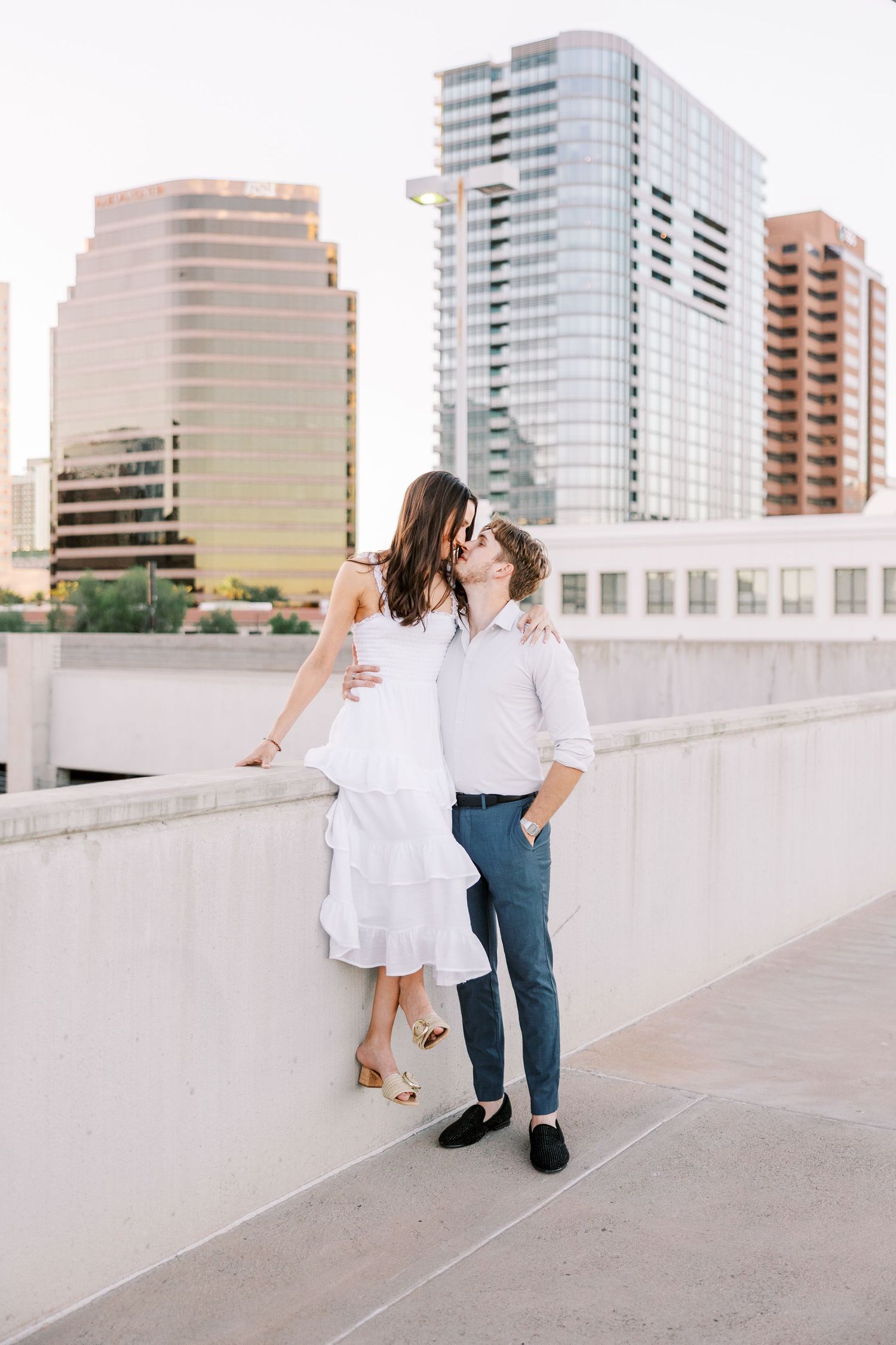 Couple walking along urban rooftop with city skyline in background.