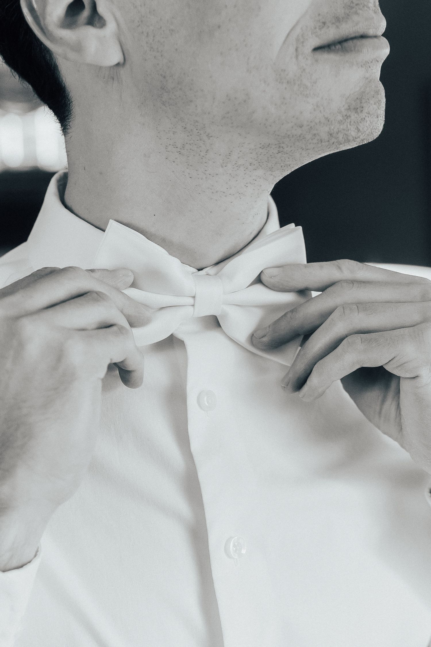 Close-up view of someone adjusting a crisp white collar shirt in monochrome.