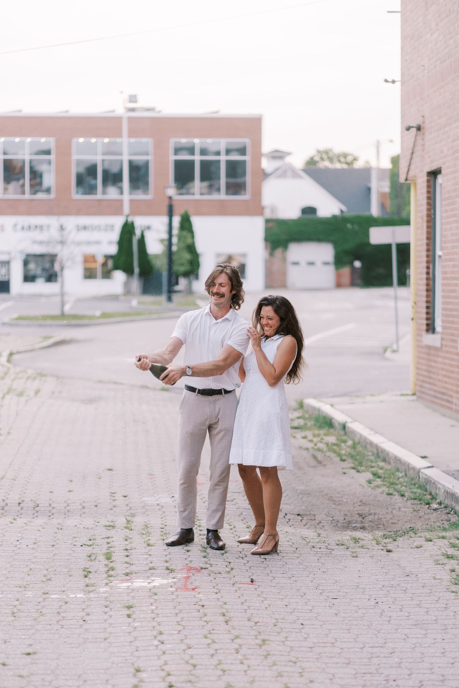 A couple shares a playful moment together on a brick pathway outside a building.