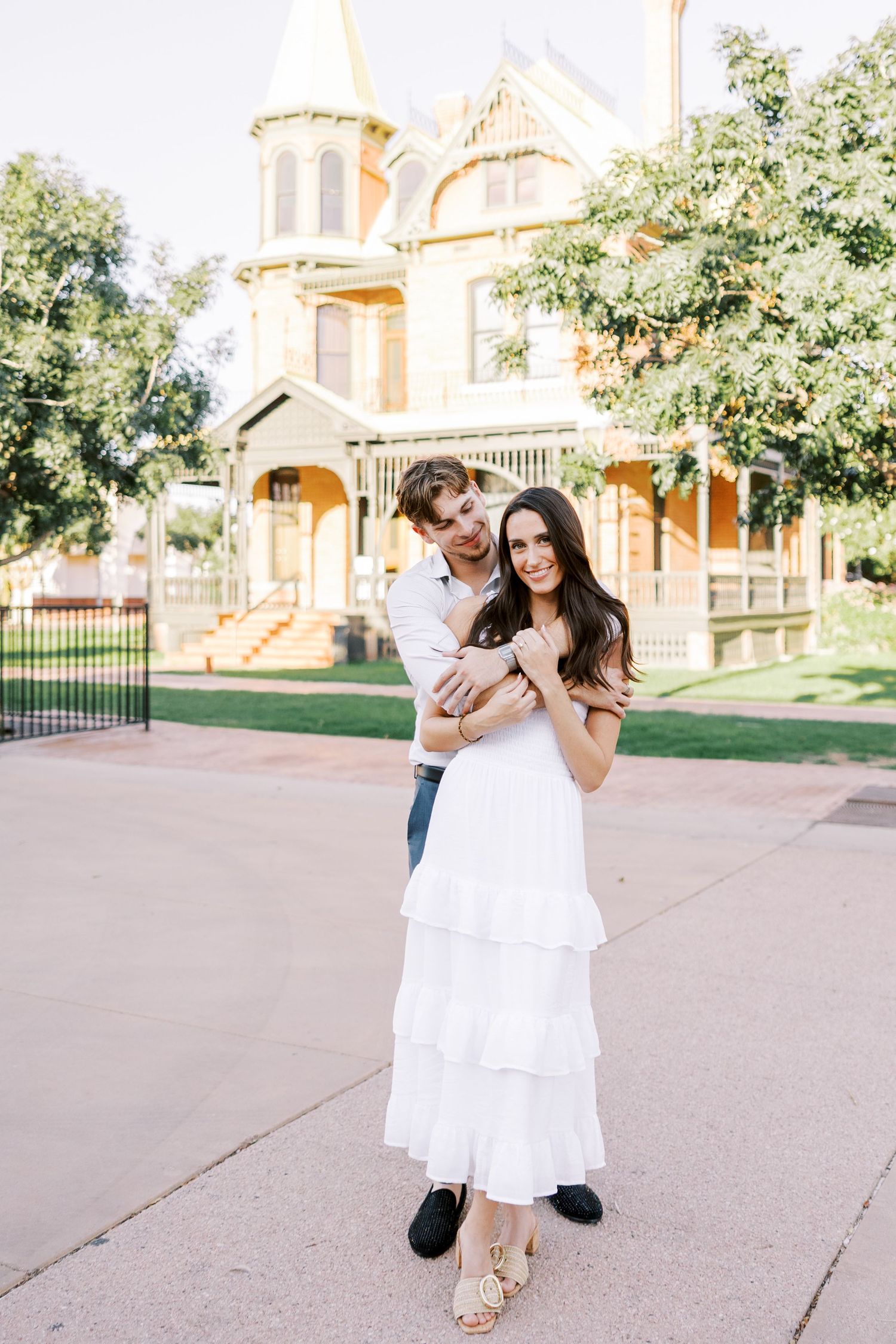 Couple walking and laughing together on a paved path with historic buildings in the background.