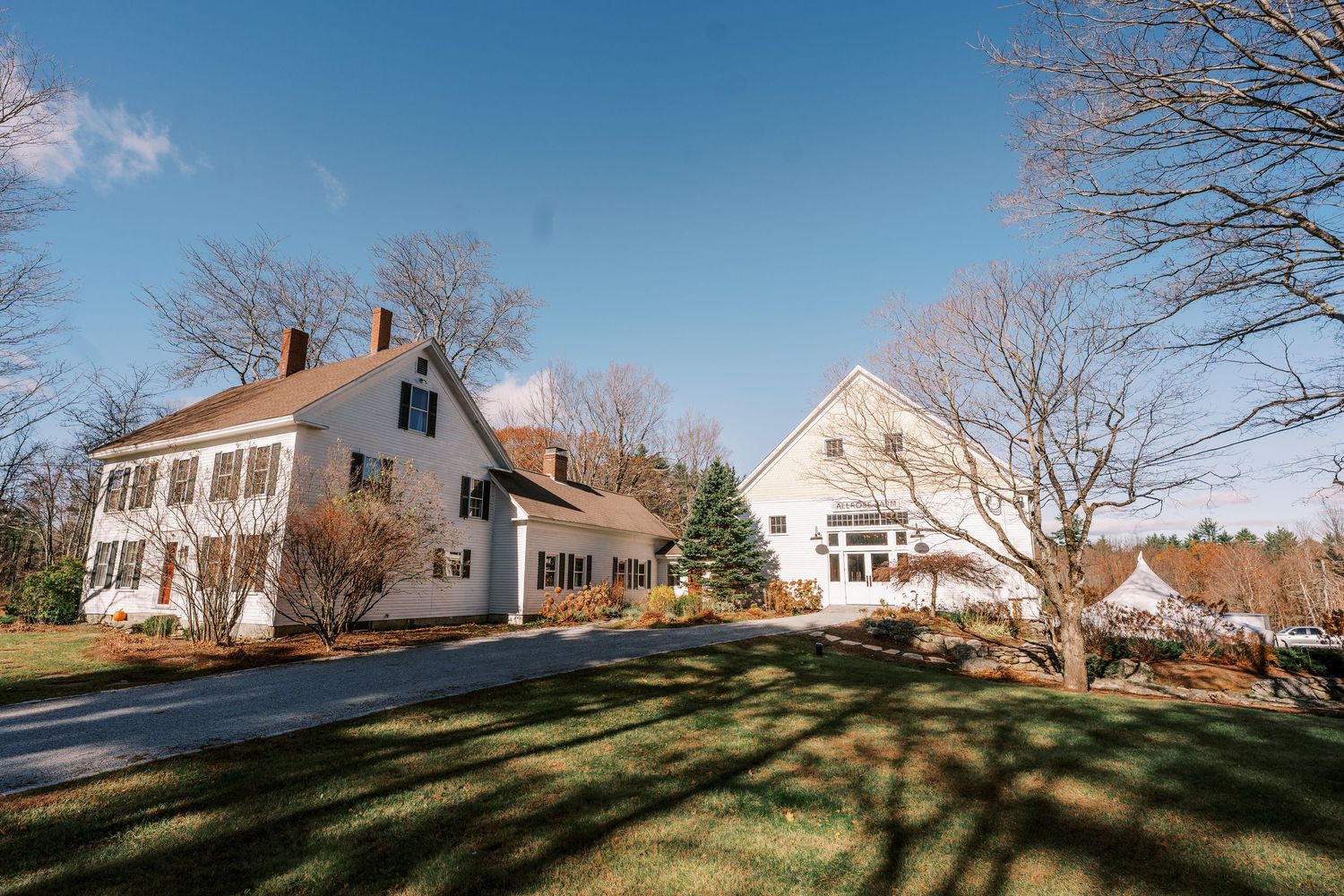 Classic white New England colonial style home with dormers and additions set on a sunny hillside lawn.