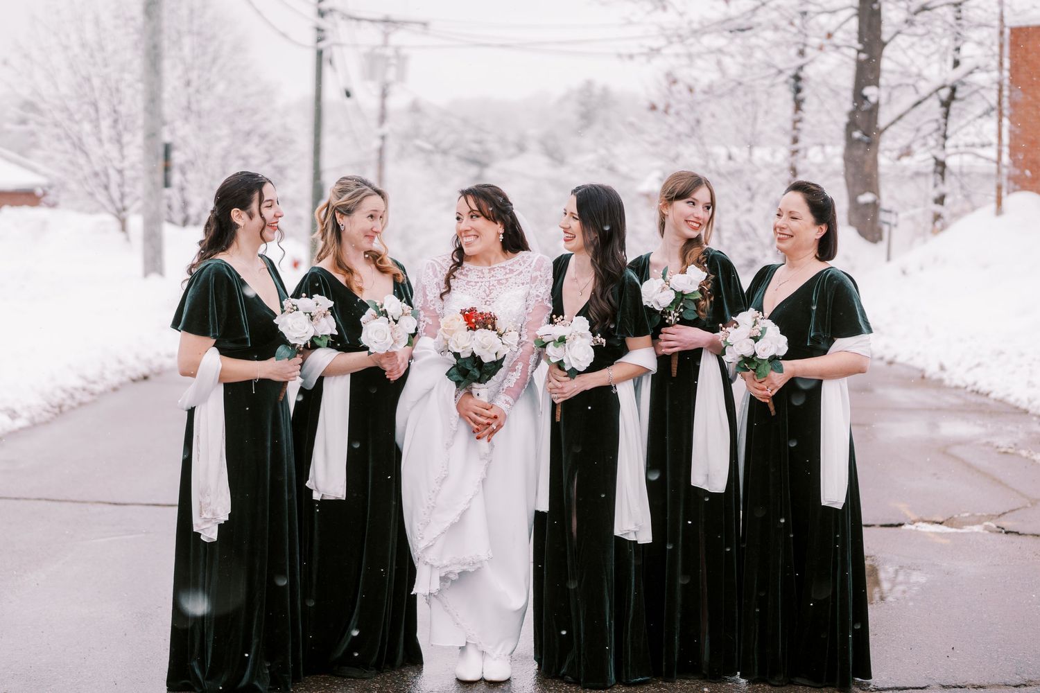 Wedding party members in black and white attire pose together in a snowy winter landscape.