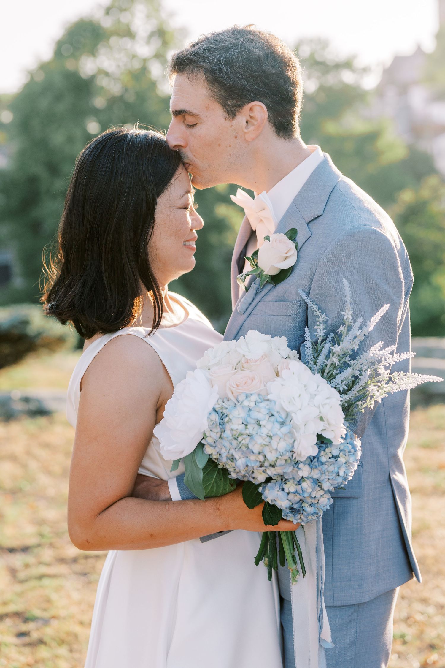 Couple shares a romantic moment with blue hydrangea bouquet during sunset photo session.