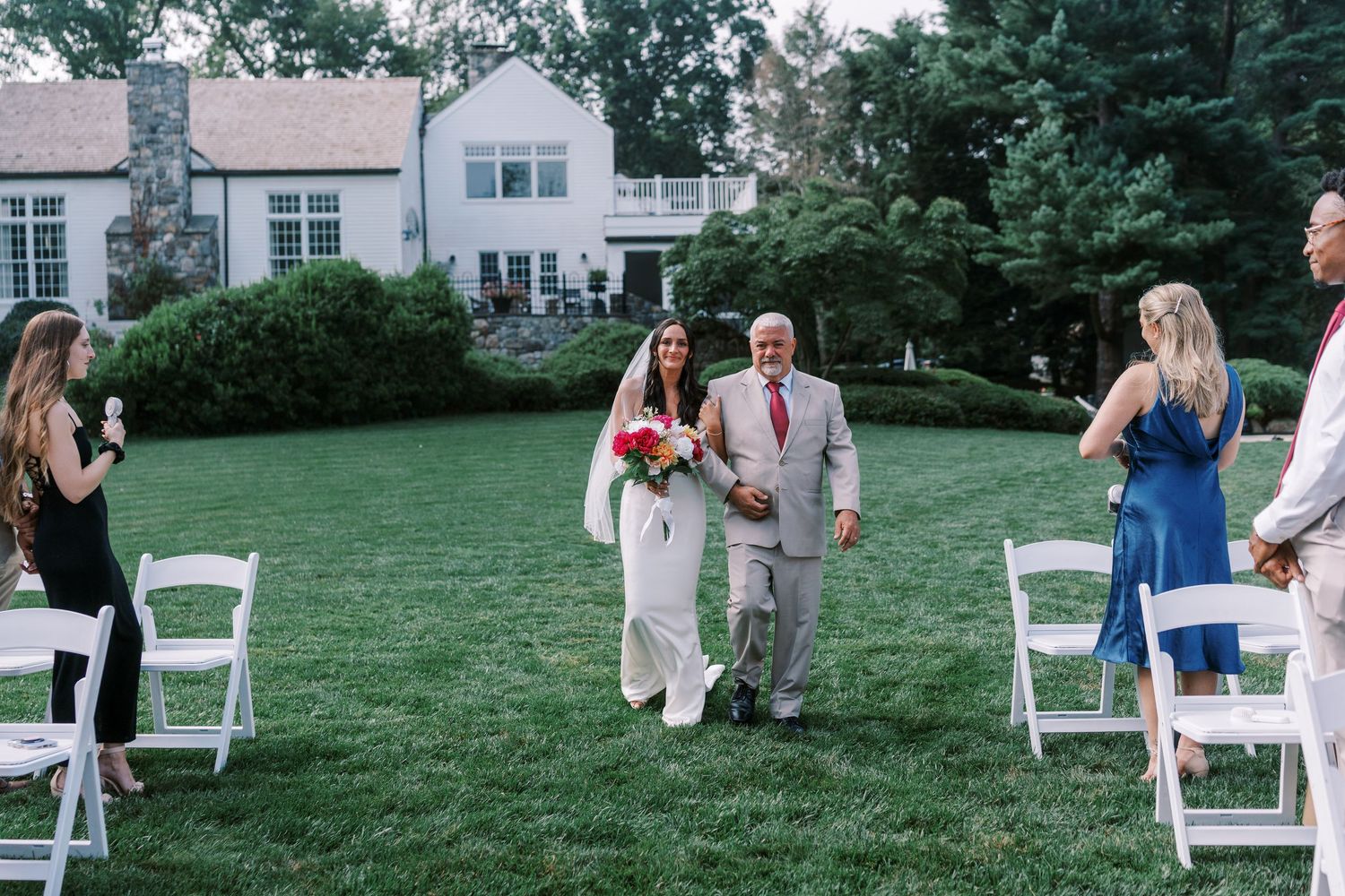 Outdoor wedding ceremony setup with white chairs arranged on a green lawn.