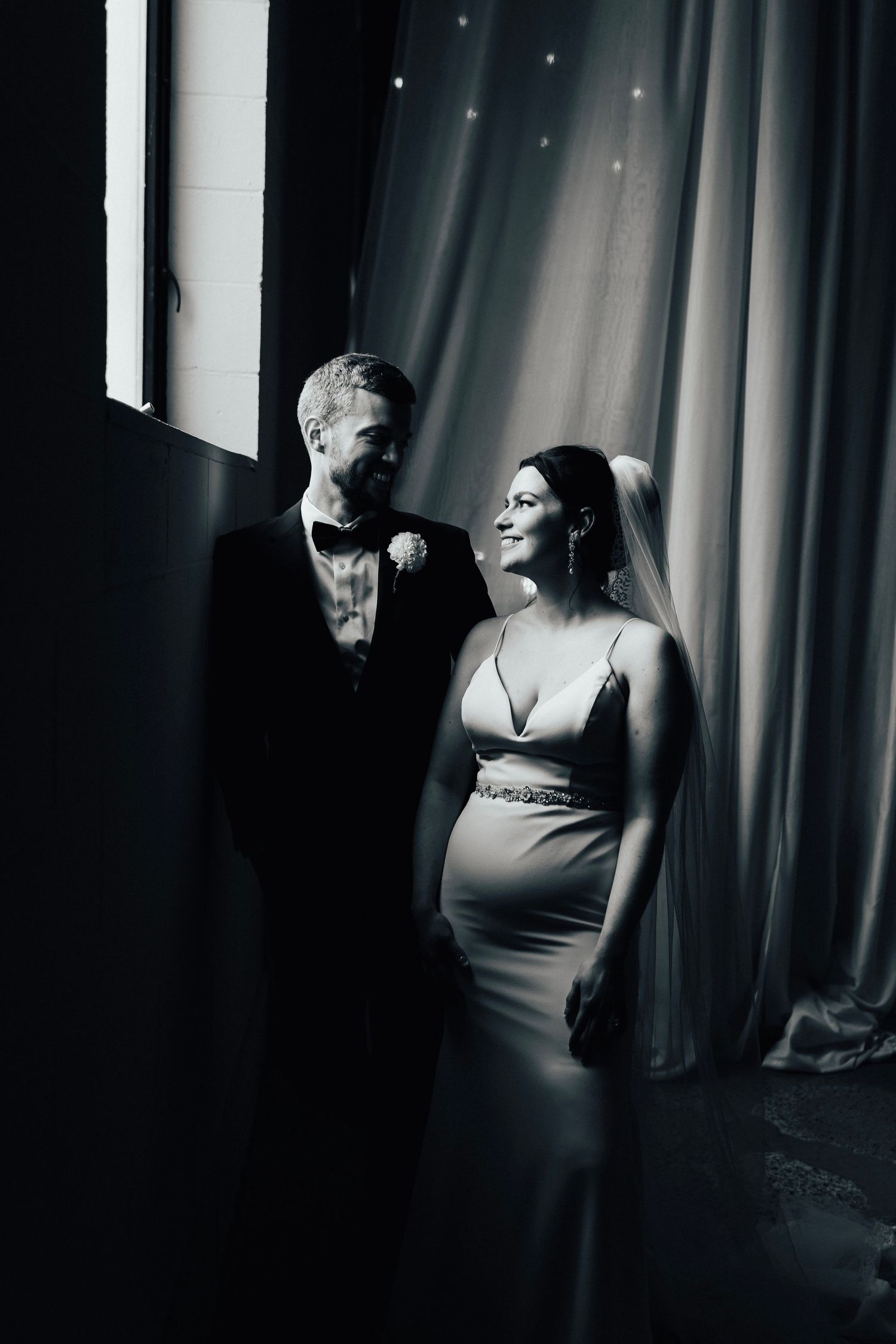 Artistic black and white wedding portrait with dramatic window lighting.