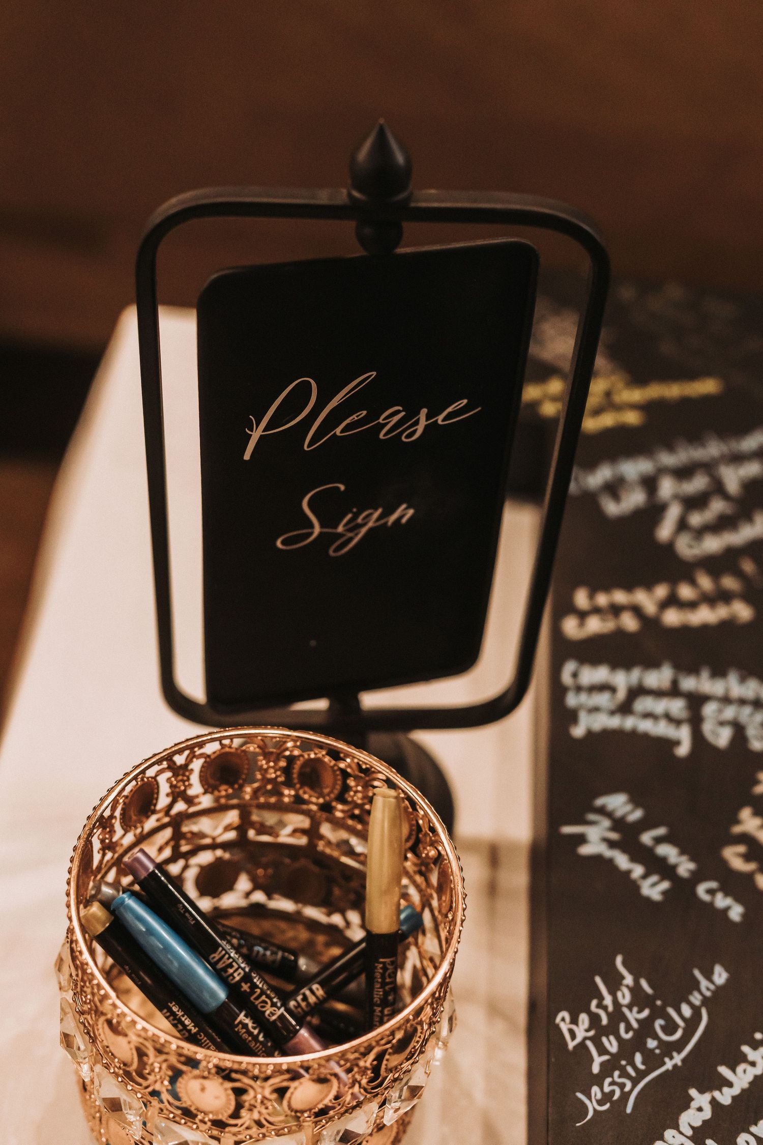 Elegant gold pen holder with a black 'Please Sign' sign at a wedding guest book station.