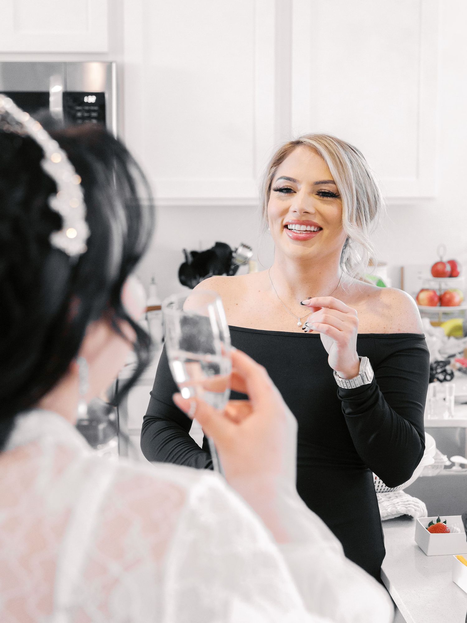 Two women with drinks engage in conversation at a social gathering in a bright modern kitchen setting.