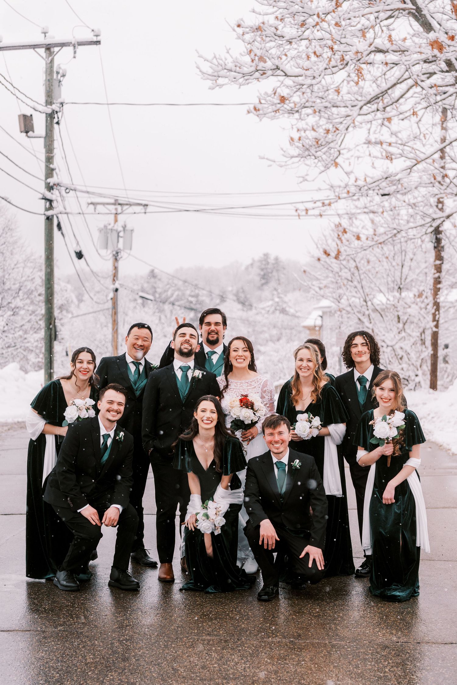 Wedding party poses playfully in the snow under cherry blossom trees.