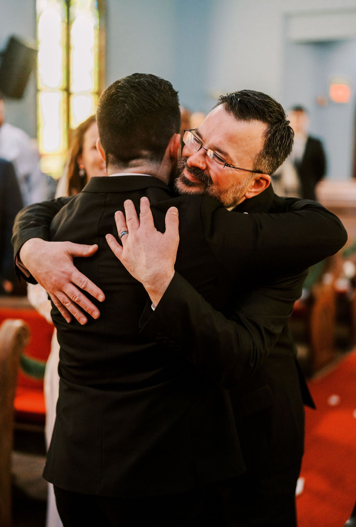 Emotional embrace between wedding party members wearing black formal attire.