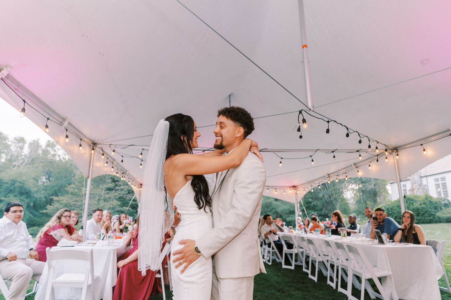Wedding reception under a white tent with string lights creating a romantic atmosphere.