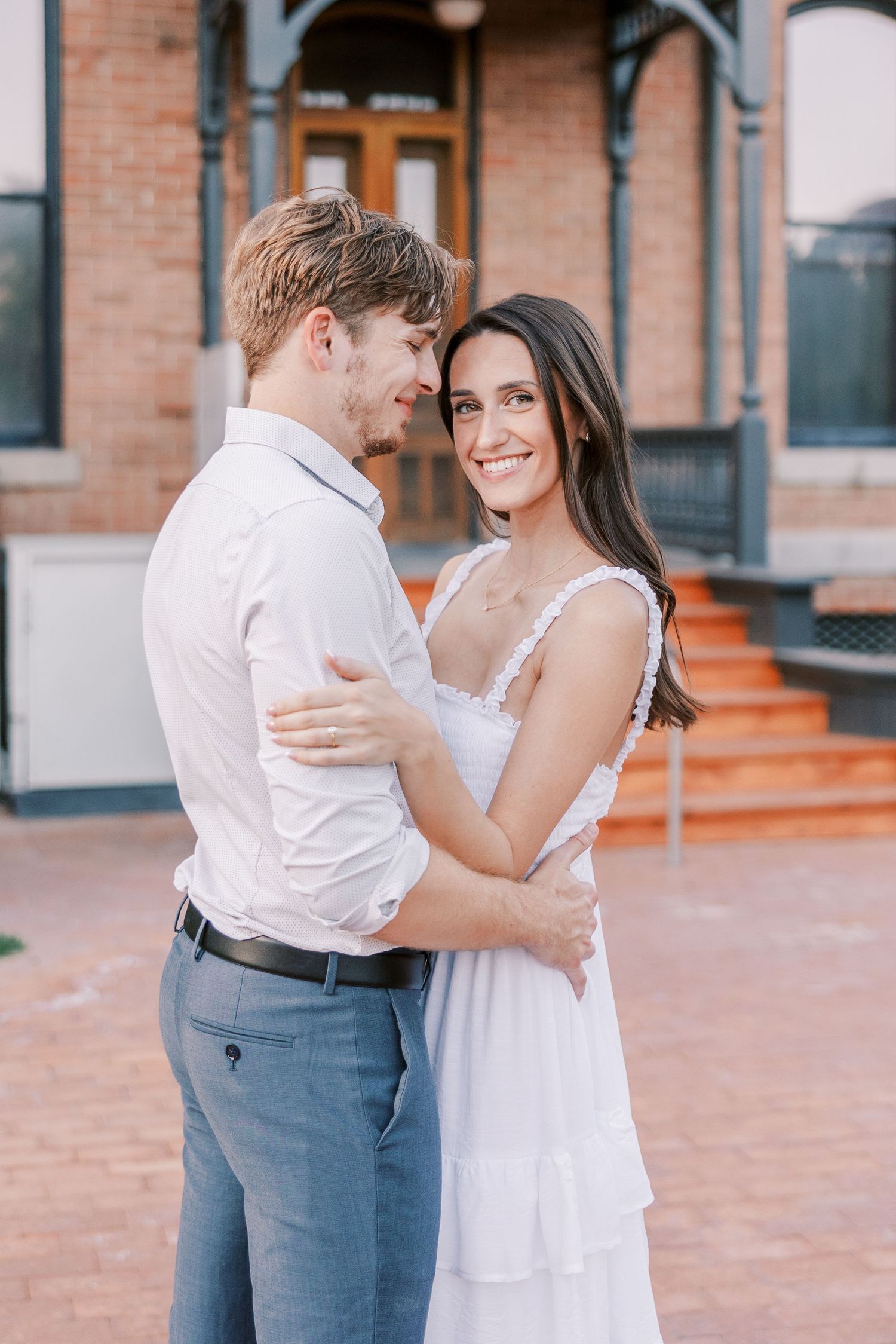 A romantic couple embracing on a brick patio outside a historic building.
