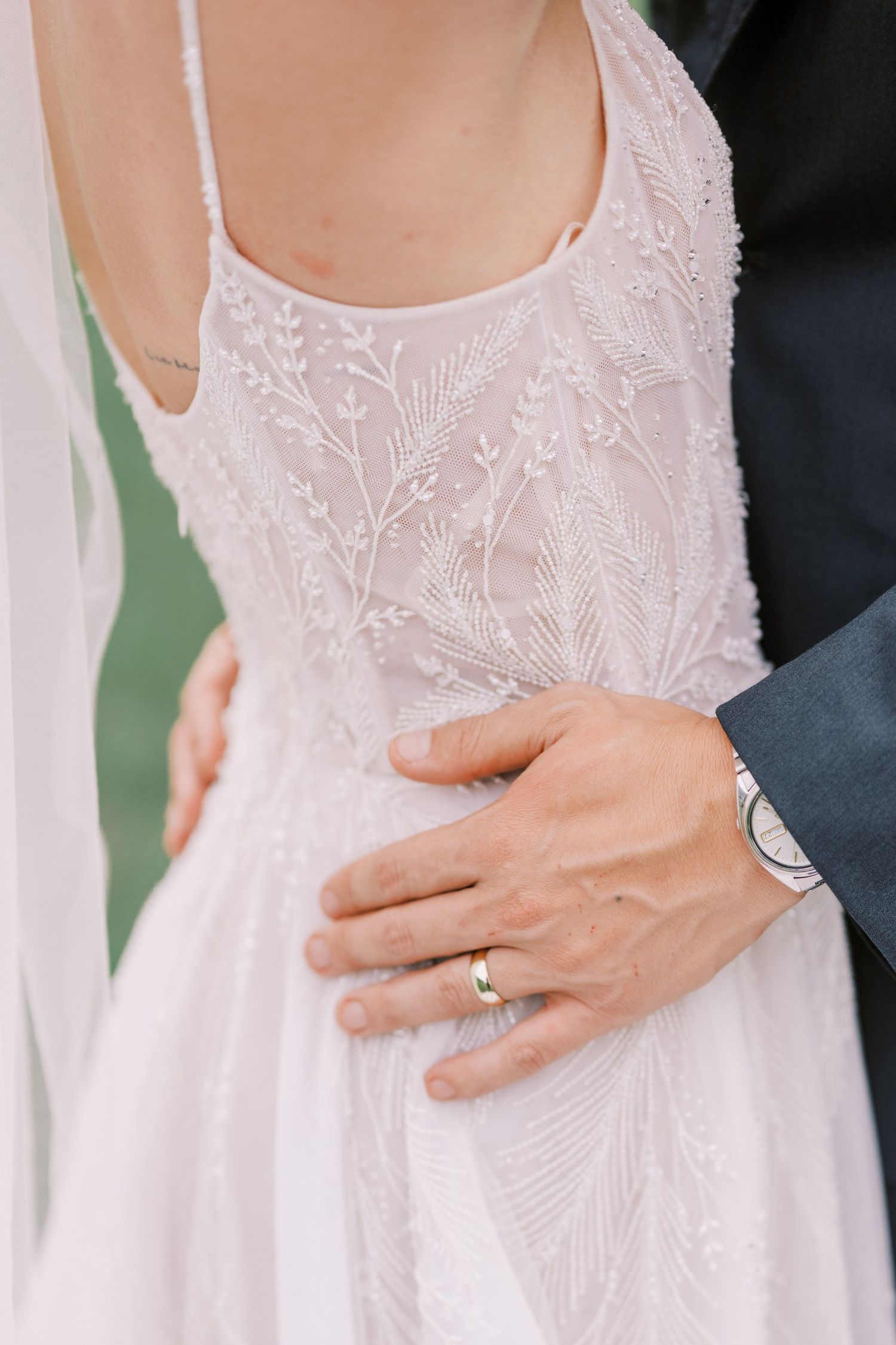Close-up of delicate lace wedding dress detail with hand wearing wedding ring.