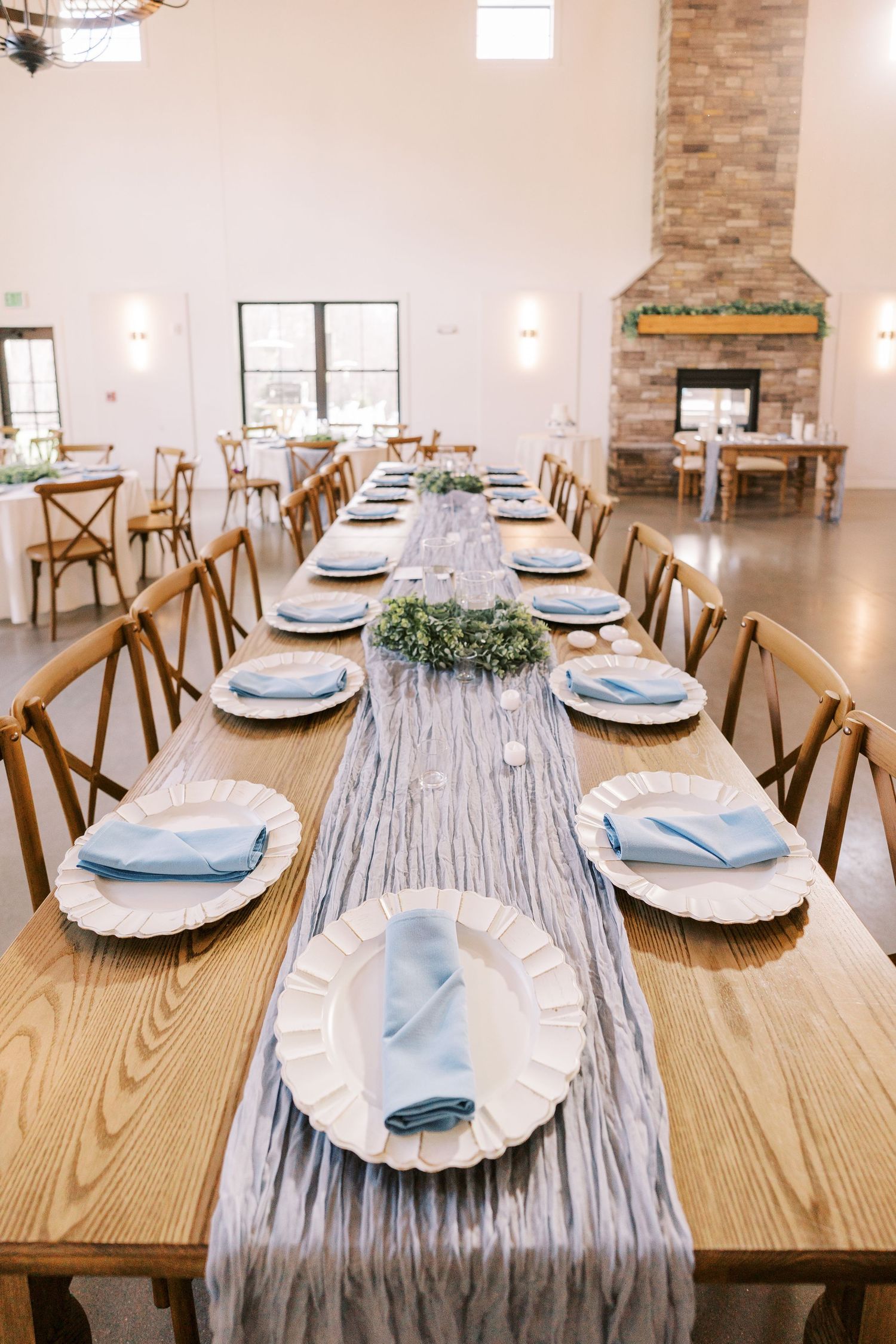 Long wooden dining table set with light blue napkins and rustic place settings in an elegant event space.