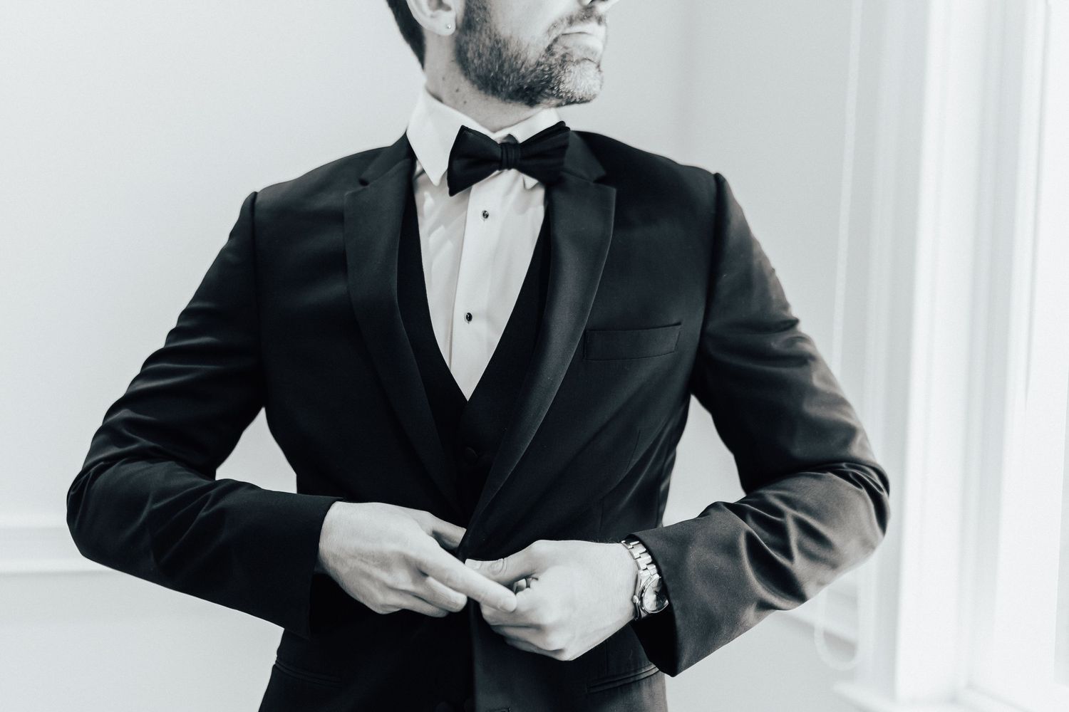 Monochromatic shot of a groom adjusting his elegant black tuxedo jacket with bow tie.