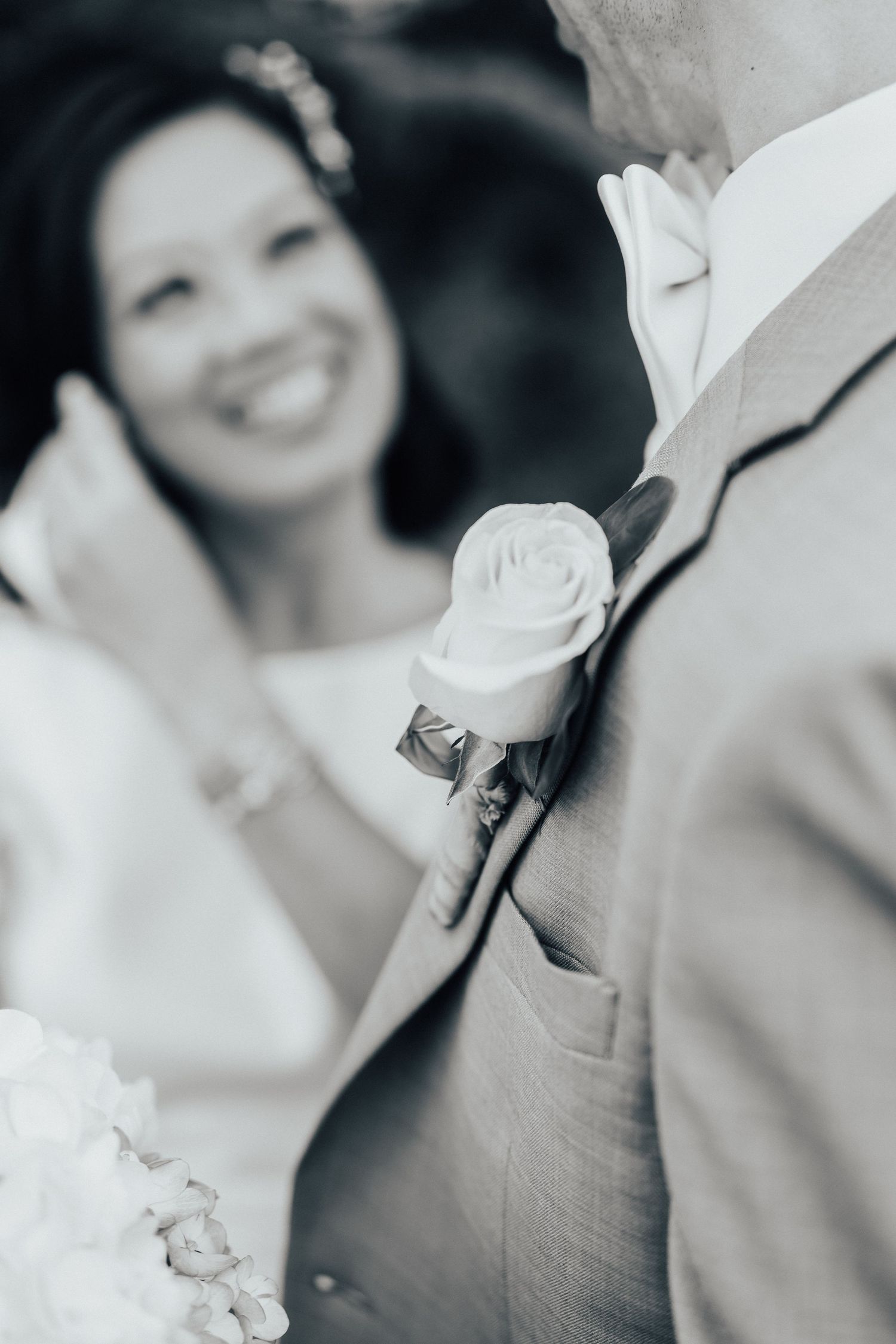 Close-up of a white rose boutonniere on a light gray suit jacket.
