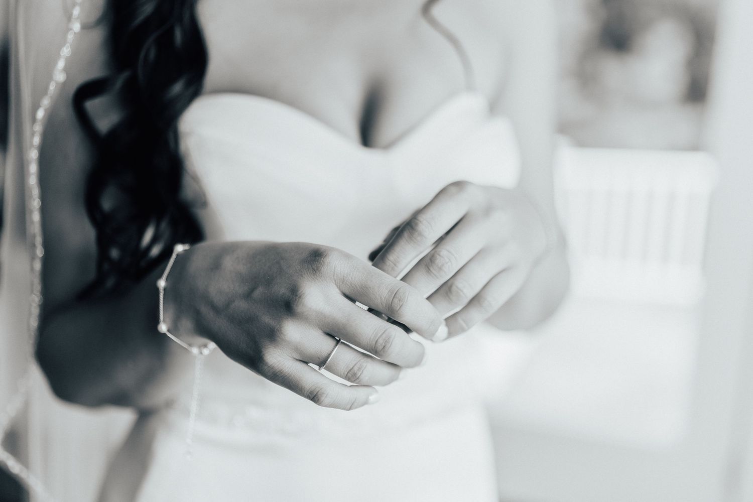 A close-up black and white photo showing wedding rings and hands against a white dress.